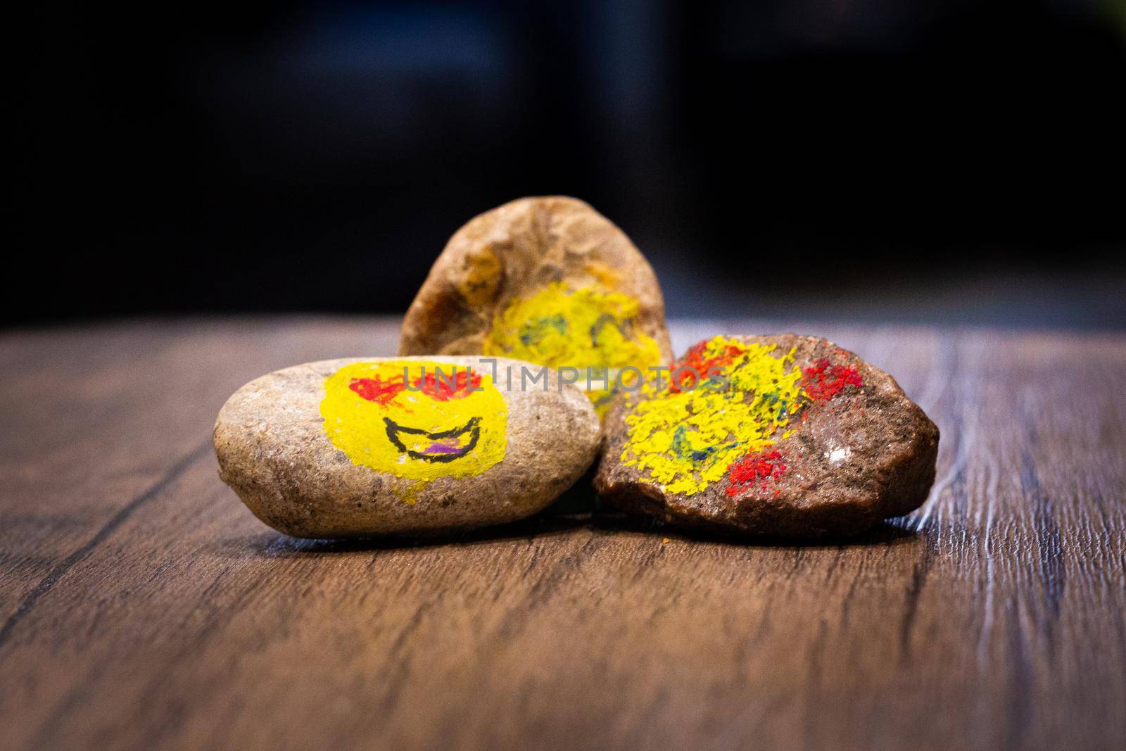 A group of three painted pebbles with emoji faces on a table