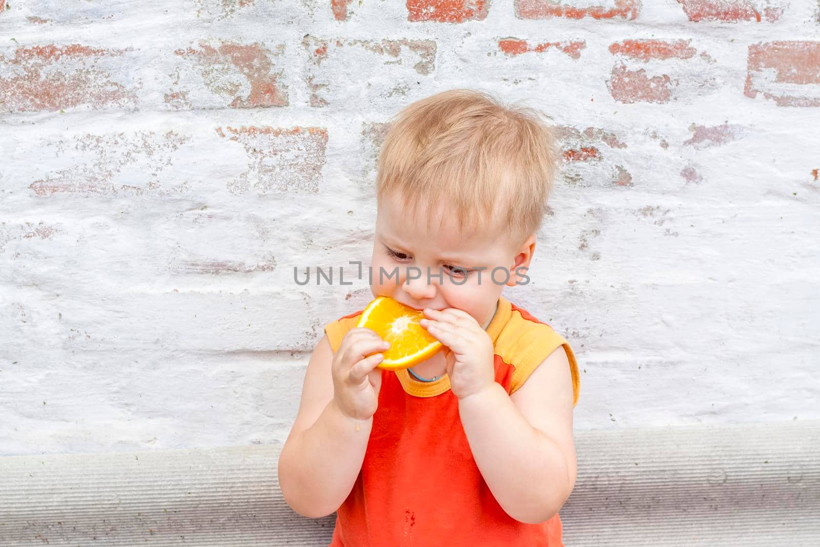 Portrait of child. Cute boy posing with an orange. The emotions of a child. Portrait of a boy against a brick wall. 