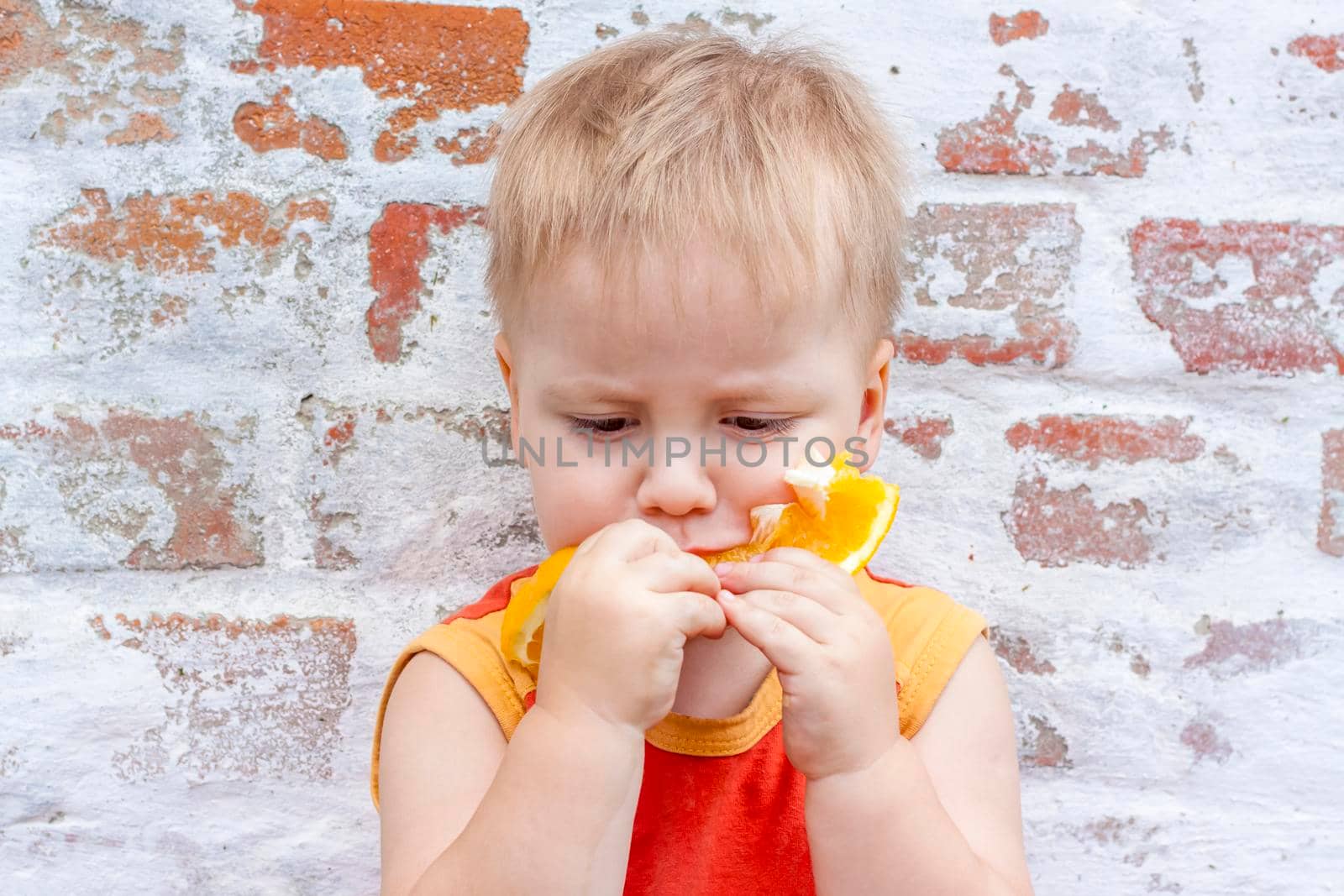 Portrait of child. Cute boy posing with an orange. The emotions of a child. Portrait of a boy against a brick wall. 