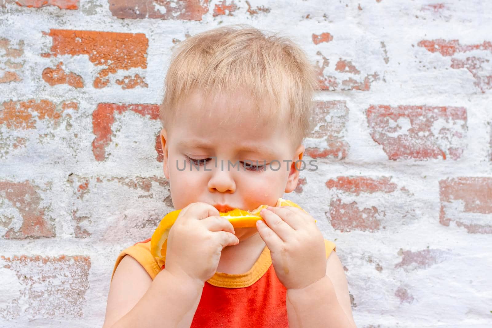 Portrait of child. Cute boy posing with an orange. The emotions of a child. Portrait of a boy against a brick wall.