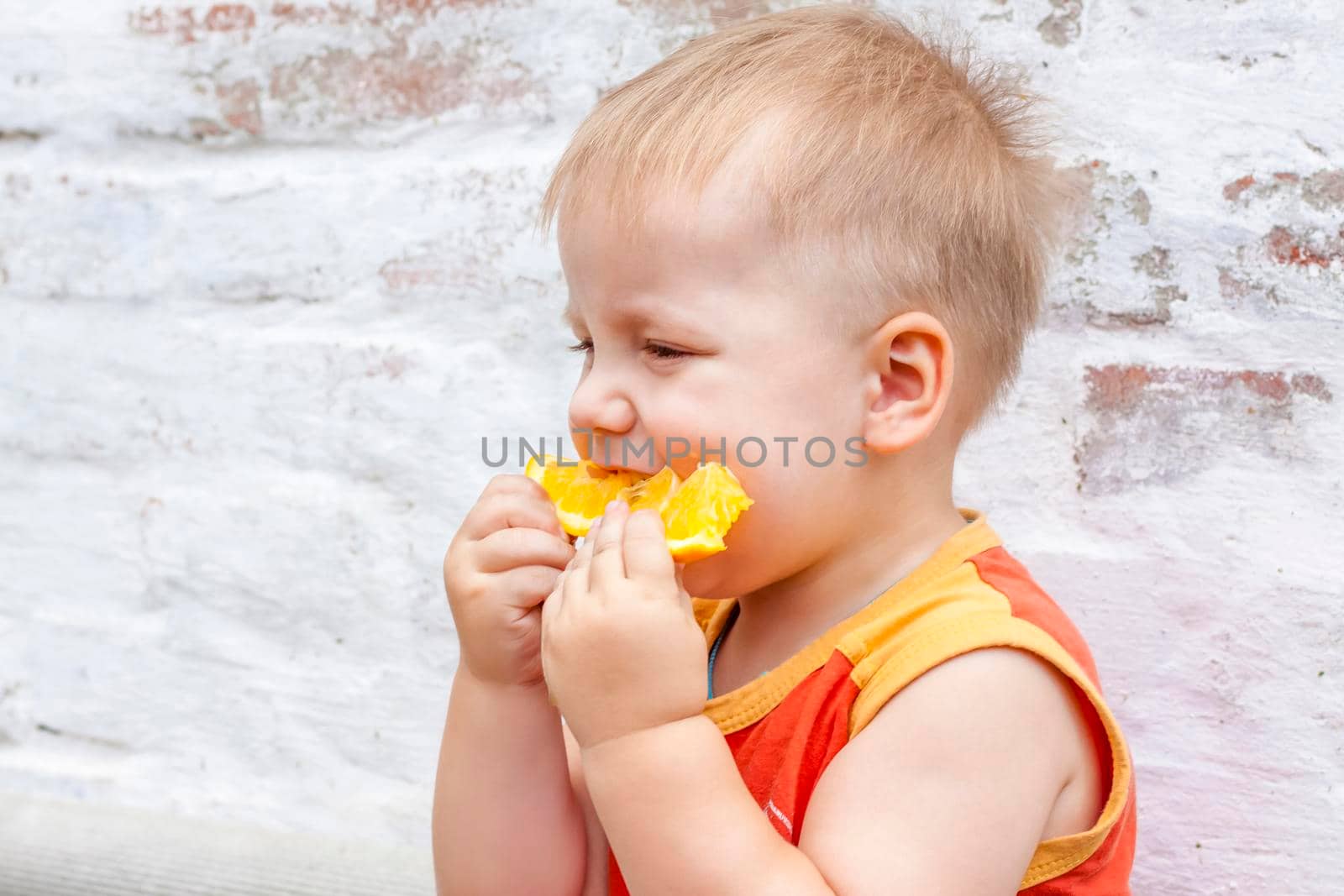 Portrait of child. Cute boy posing with an orange. The emotions of a child. Portrait of a boy against a brick wall.