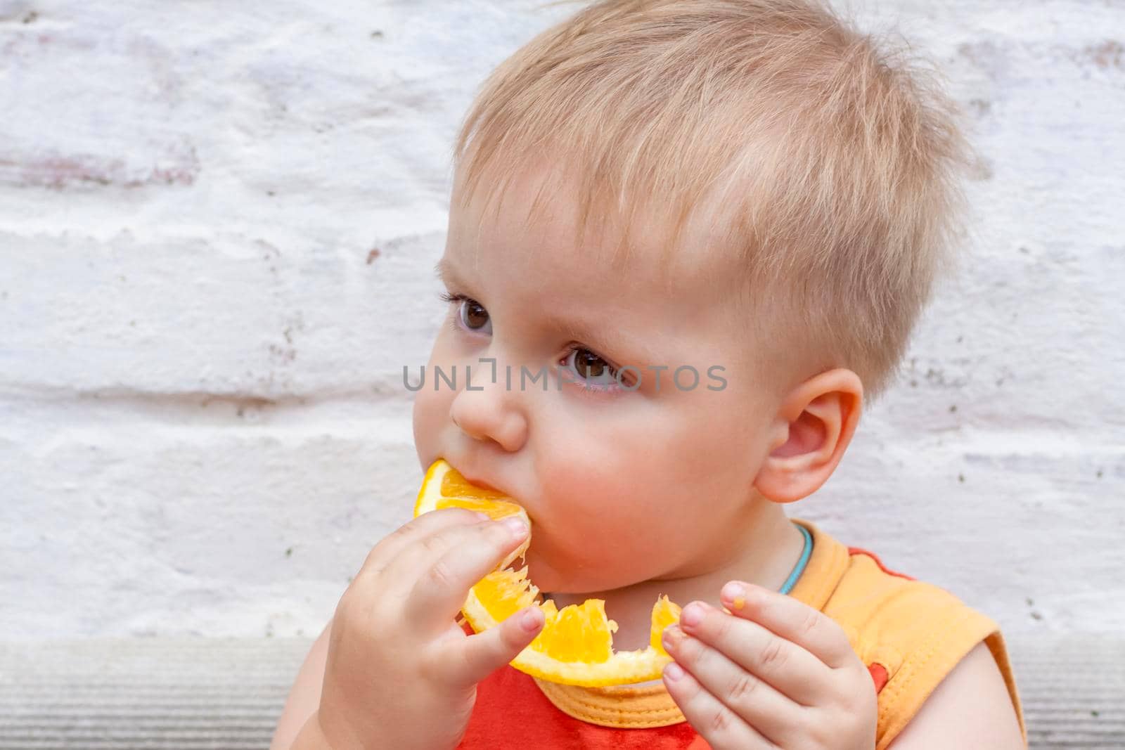 Portrait of child. Cute boy posing and eating a delicious orange. The emotions of a child. Portrait of child. Boy on the background of a brick wall.      