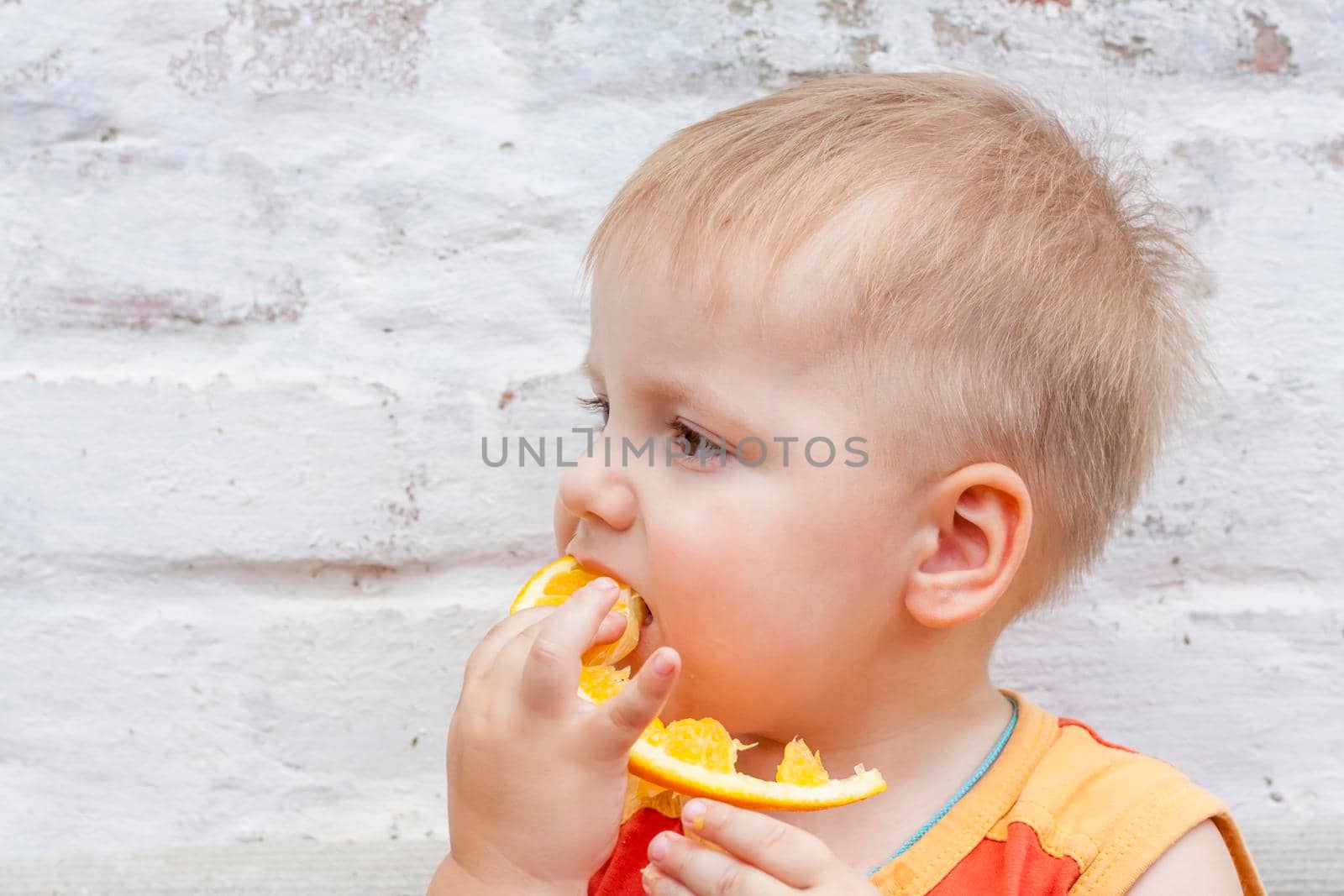 Portrait of child. Cute boy posing and eating a delicious orange. The emotions of a child. Portrait of child. Boy on the background of a brick wall.  