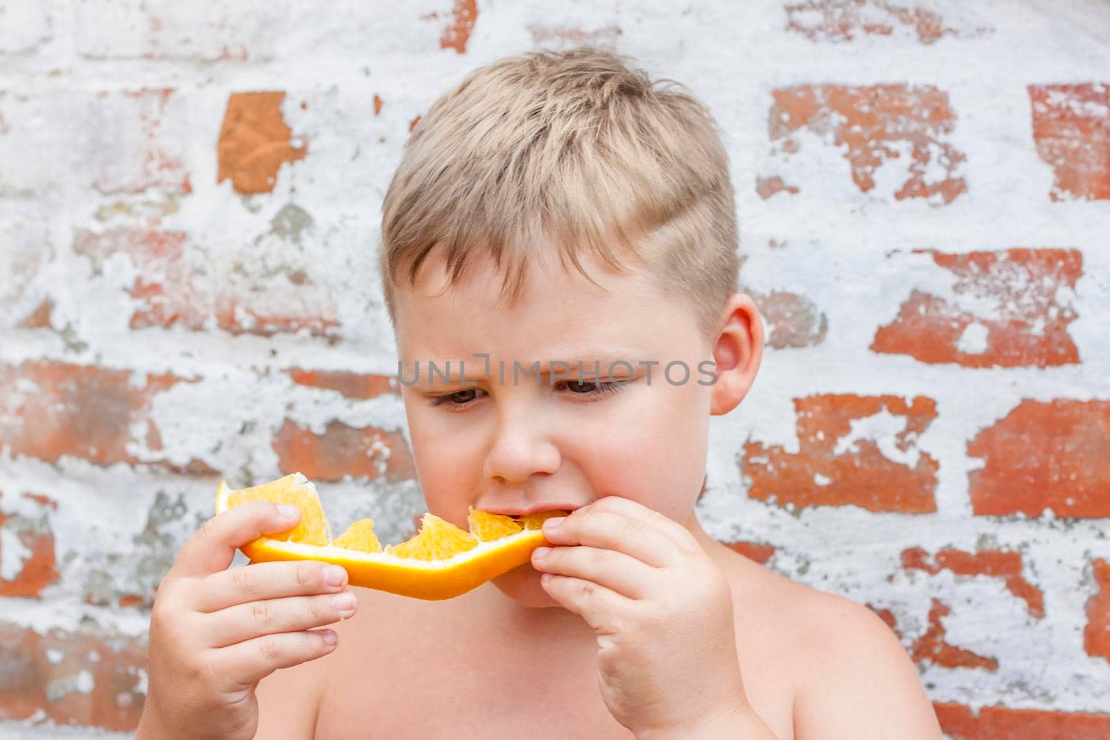 Portrait of child. Cute boy posing and eating a delicious orange. The emotions of a child. Portrait of child. Boy on the background of a brick wall.  