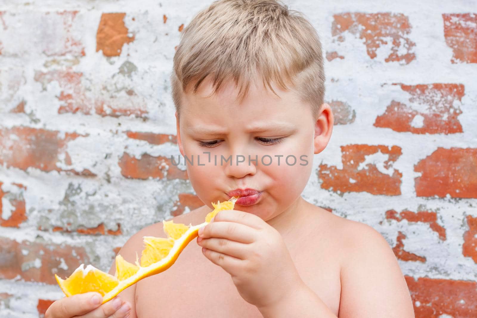 Portrait of child. Cute boy posing and eating a delicious orange. The emotions of a child. Portrait of child. Boy on the background of a brick wall.    