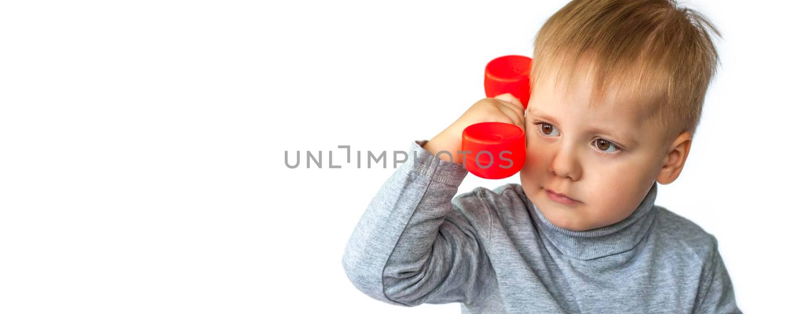 Portrait of a surprised cute little boy holding a red telephone receiver. The child is isolated on a white background. The concept of an advertising banner. Emergency call. Phone call. Phone in hand. 