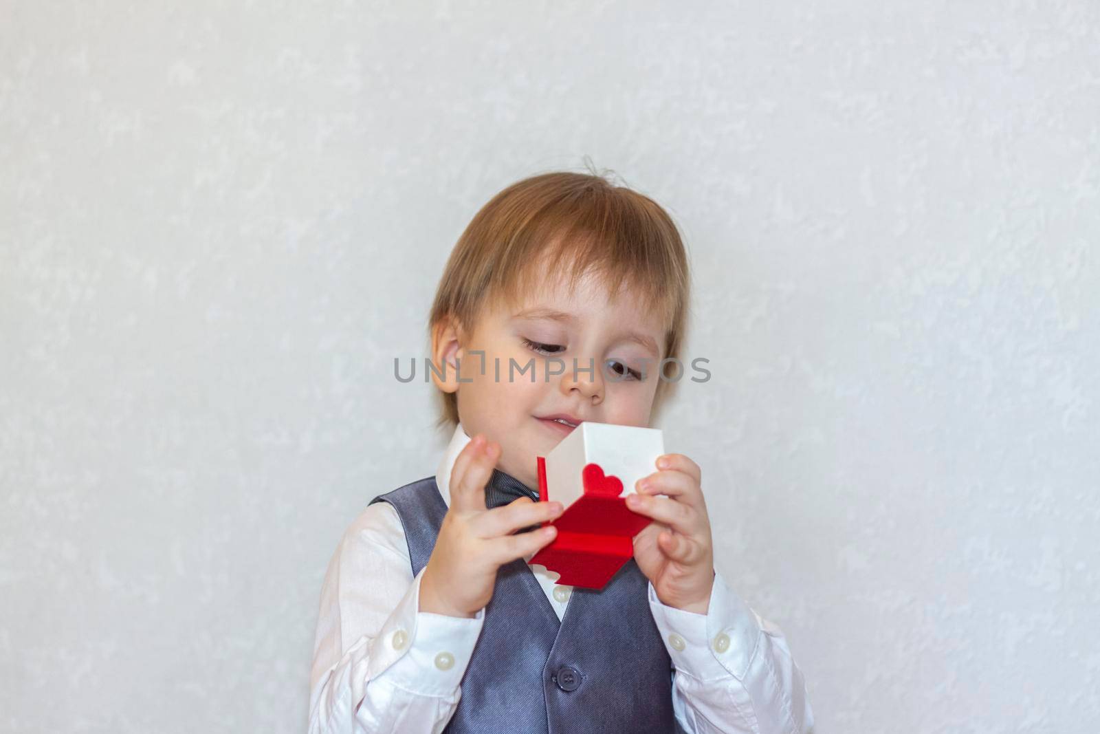 A little boy holds and hands over a red box, a Valentine's Day theme concept. Portrait of a cute boy in a suit with a bow tie. Valentine's Day. 