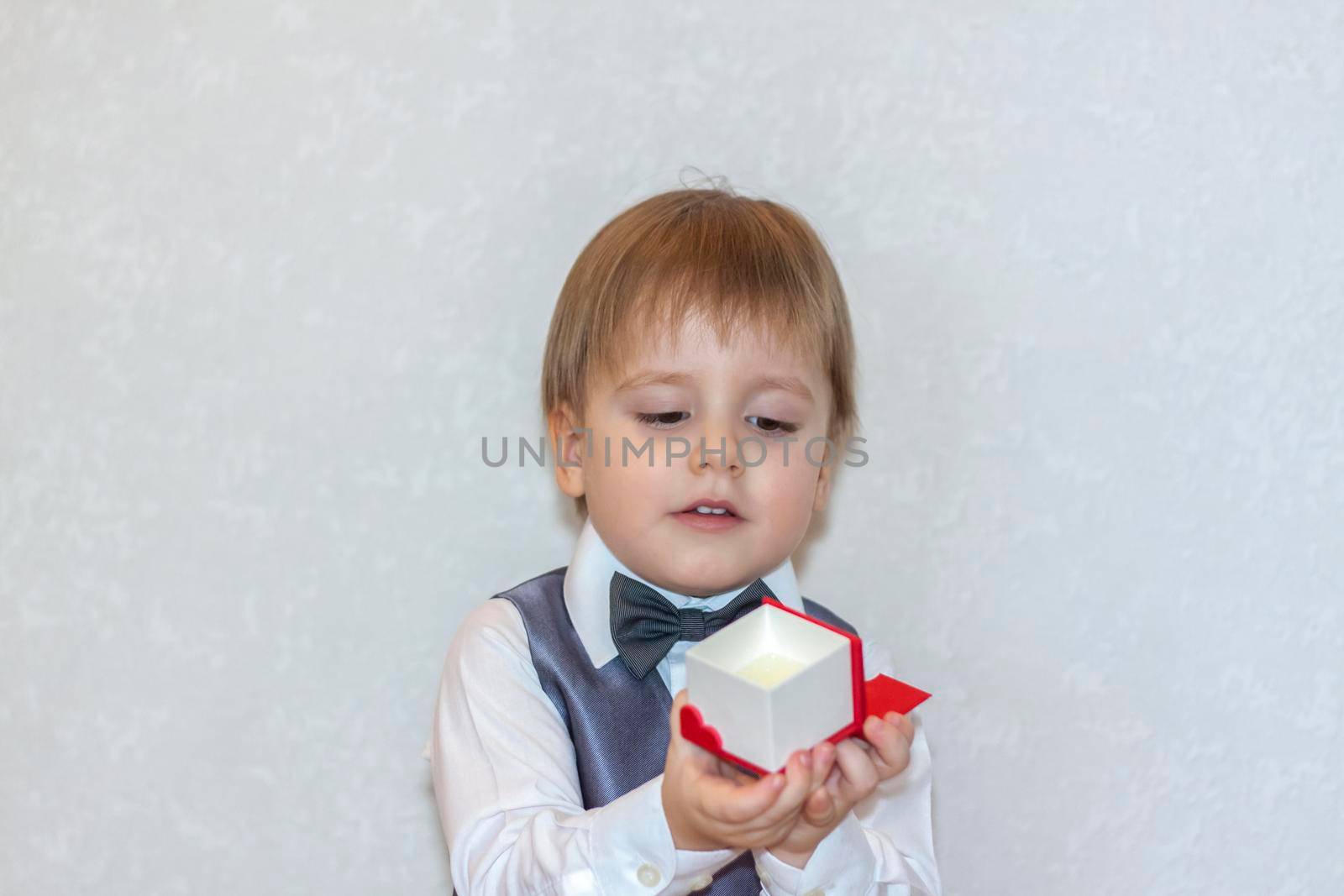 A little boy holds and hands over a red box, a Valentine's Day theme concept. Portrait of a cute boy in a suit with a bow tie. Valentine's Day.