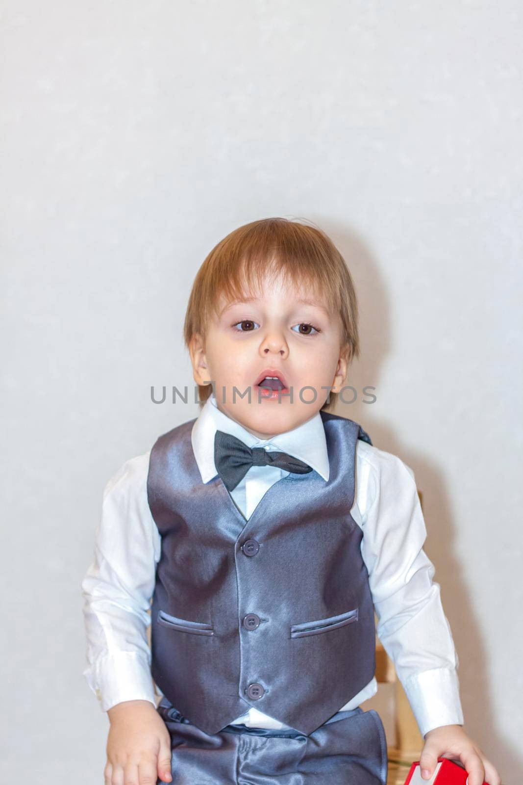 A little boy holds and hands over a red box, a Valentine's Day theme concept. Portrait of a cute boy in a suit with a bow tie. Valentine's Day.