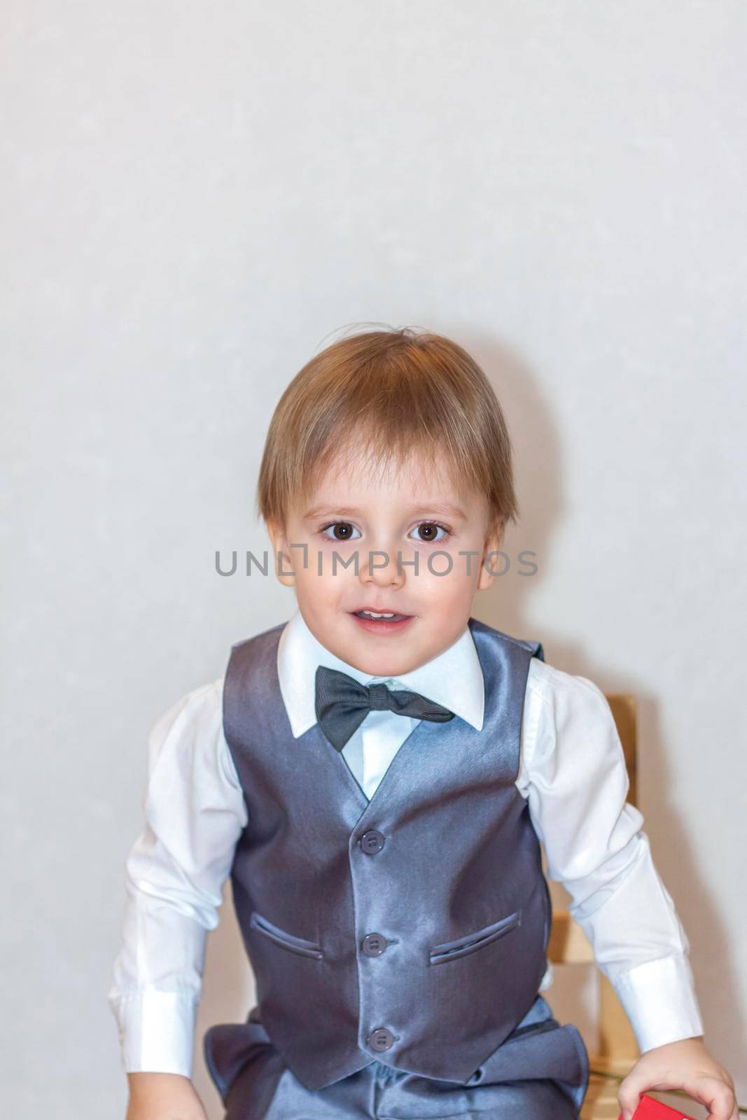 A little boy holds and hands over a red box, a Valentine's Day theme concept. Portrait of a cute boy in a suit with a bow tie. Valentine's Day. 