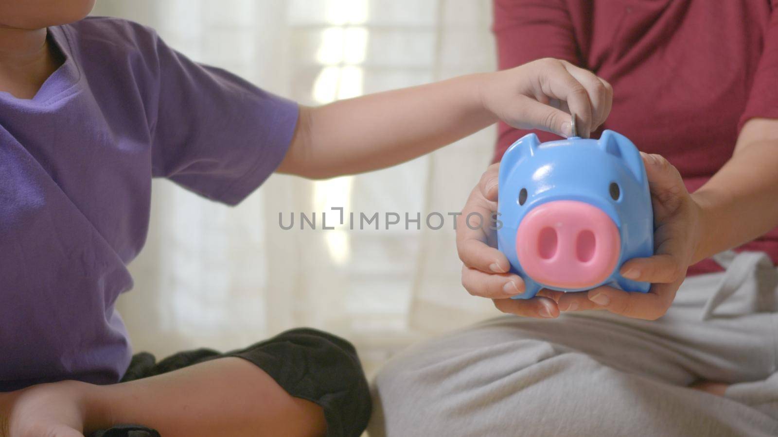 kid boy preschool putting pin money coins into blue faced piglet slot by Sorapop