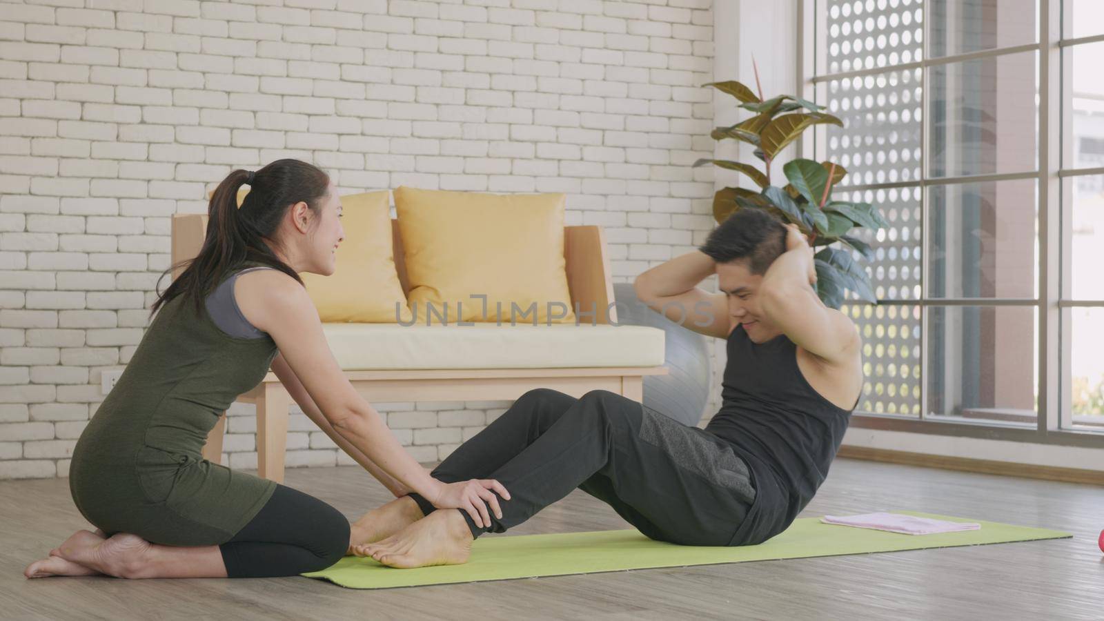 Happy Asian family couple husband and wife healthy trainer workout home in the living room. Fit man lifestyle doing sit up fitness exercise at home on floor with girlfriend support helping boyfriend
