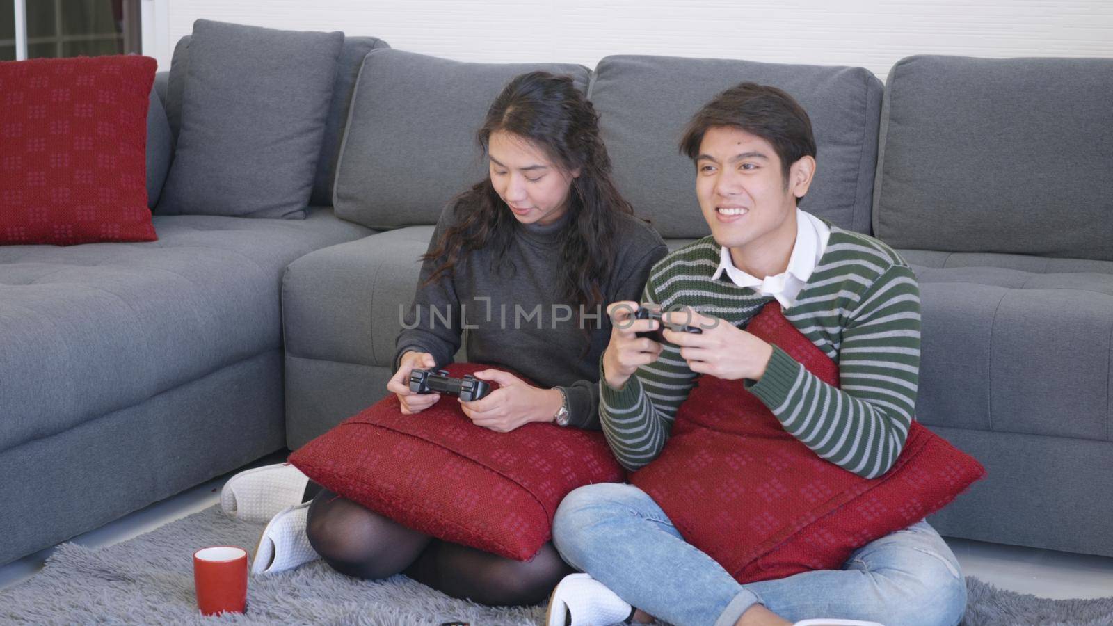 Happy Asian beautiful young family couple husband and wife smile and laugh enjoying funny with each other playing video game, holding joysticks console. Happiness and gaming concept.