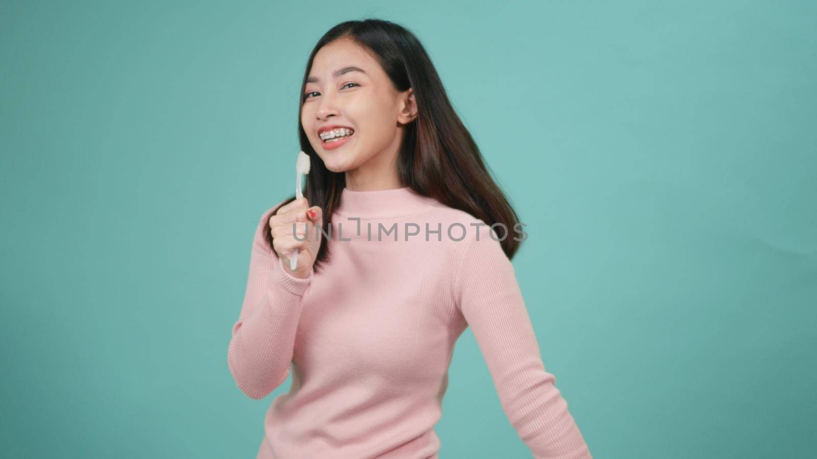 Asian young beautiful woman smile brushing teeth dancing enjoying music,  Female brush teeth singing song, dance and have fun isolated on blue background, lifestyle dental hygiene and health concept