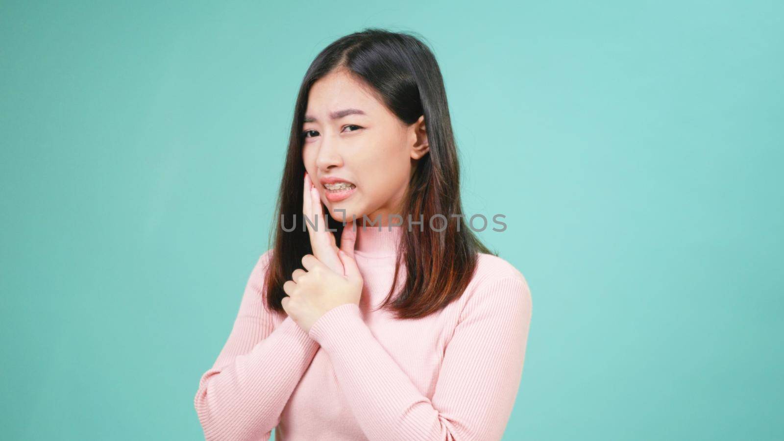 Portrait young Asian beautiful woman wear silicone orthodontic retainers on teeth feeling pain toothache holding her cheek with hand isolated on blue background. Female suffering teeth pain dental