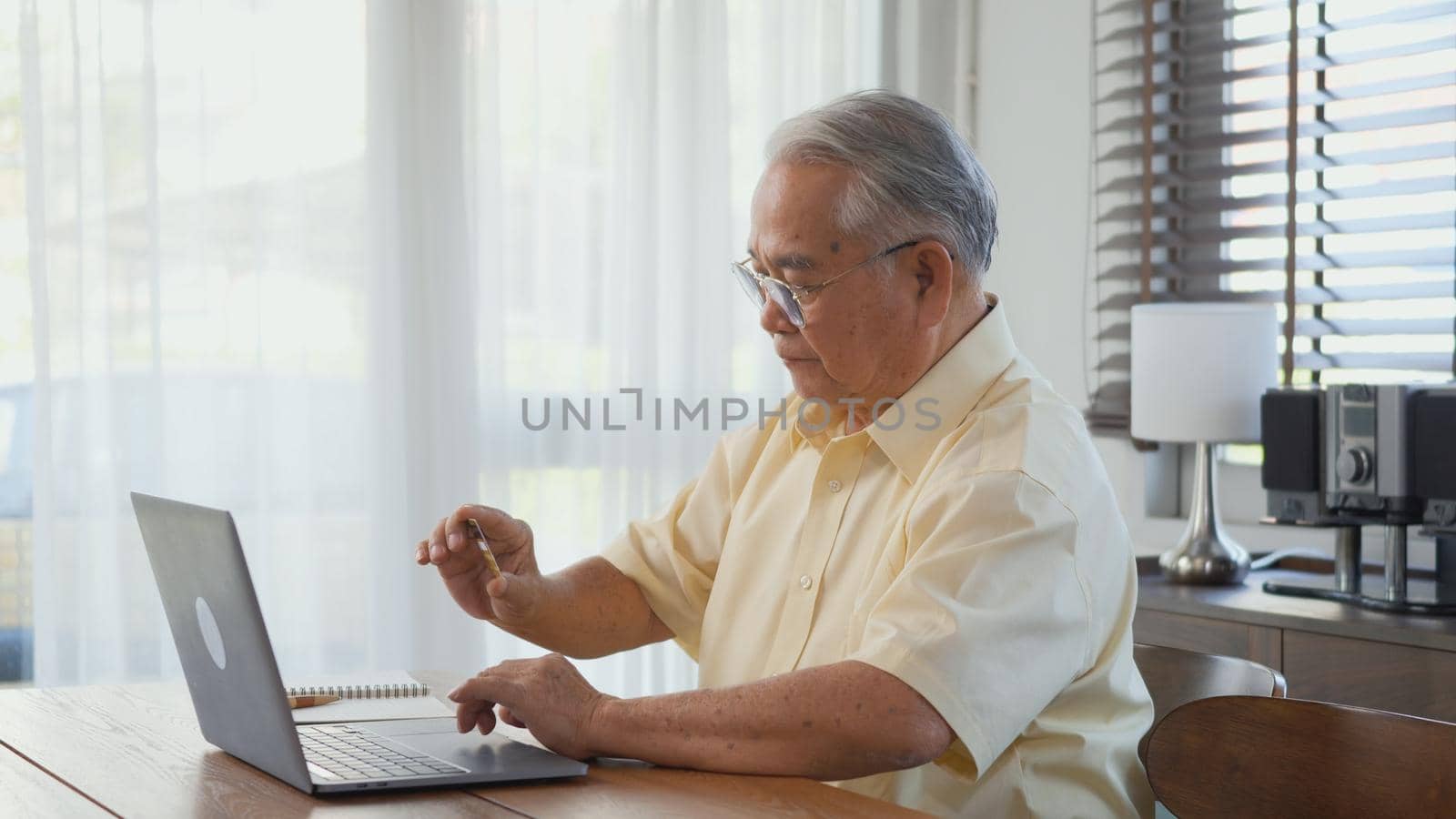 Senior man dressed wear eyeglasses sitting on chair working on laptop in living room at home, Happy old man retired using computer, Elderly grandfather work from home