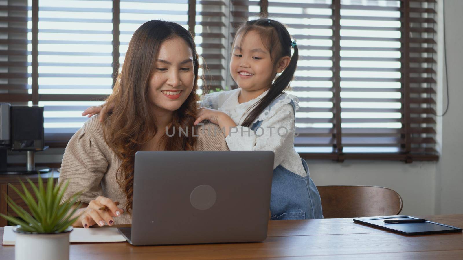 Asian young mother working with laptop computer at home his daughter help support giving shoulder massage to mother for stress relief, lifestyle freelance woman using notebook and kid help support