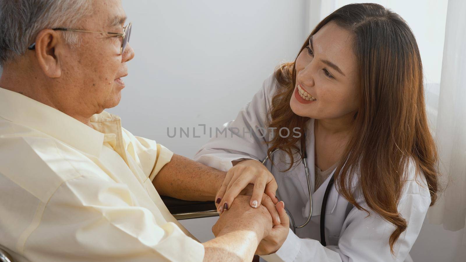 Female nurse doctor wear white uniform holding hand of patient senior or elderly old man during sit on wheelchair encourage and empathy at nursing hospital, older people healthcare support concept