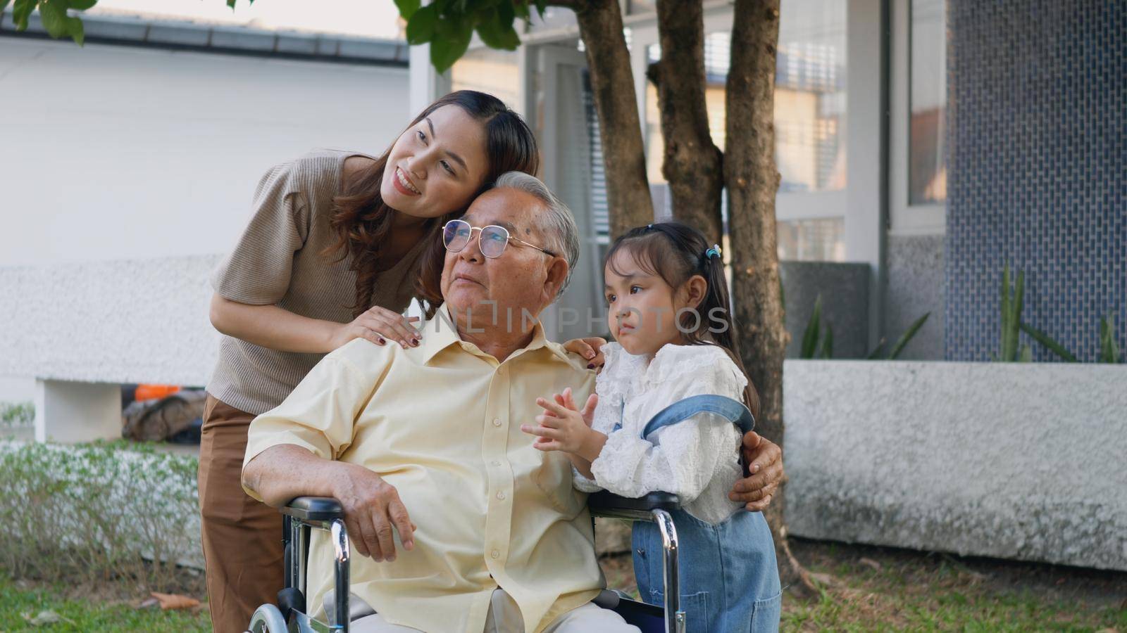 Disabled senior grandpa on wheelchair with grandchild and mother in park, Happy Asian three generation family having fun together outdoors backyard, Grandpa and little child smiling and laughed