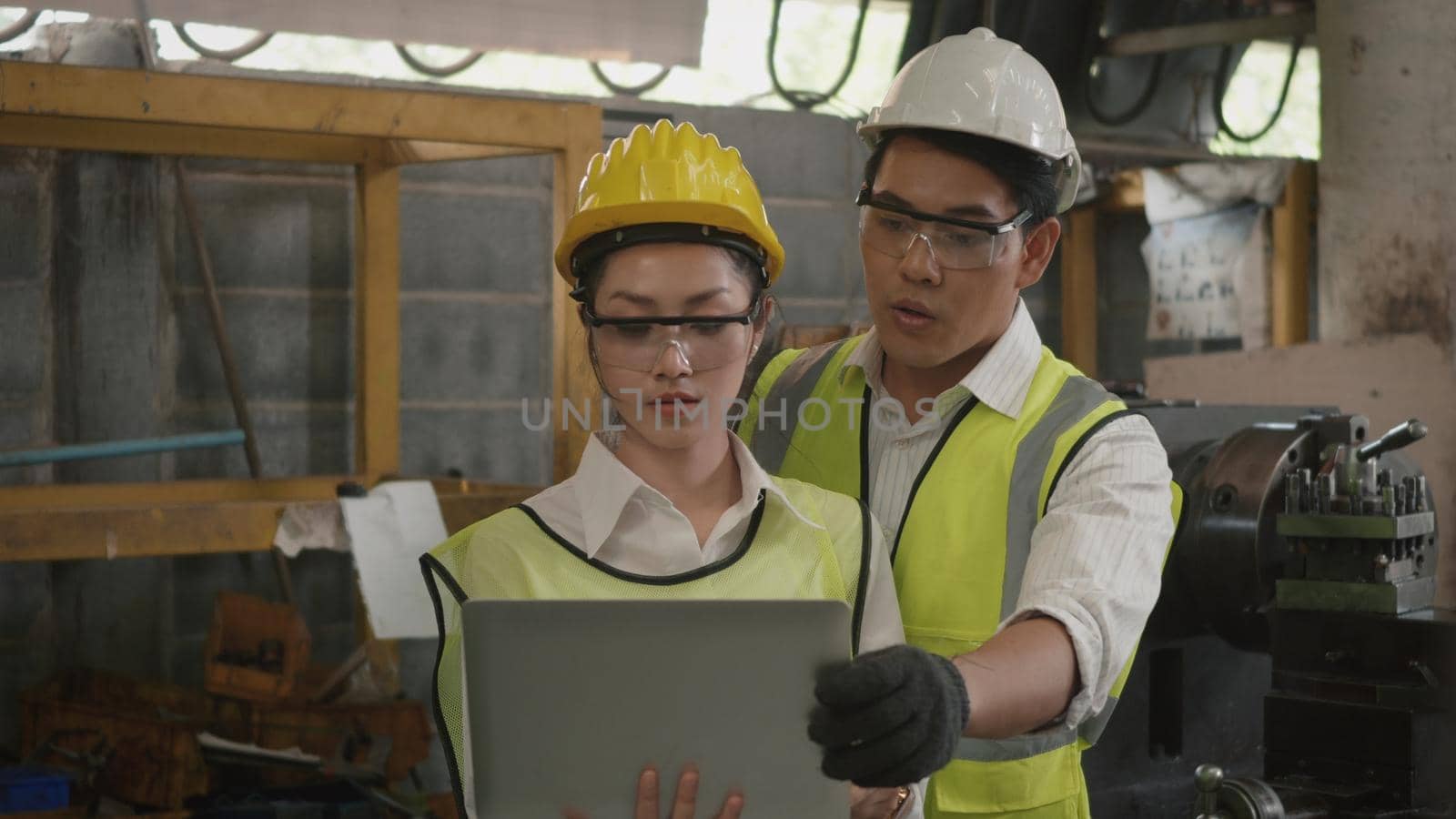 Asian professional mechanical engineer woman and operation man wearing uniform hardhat and goggles safety working on workshop metal lathe industrial manufacturing factory, Heavy industry lathe worker