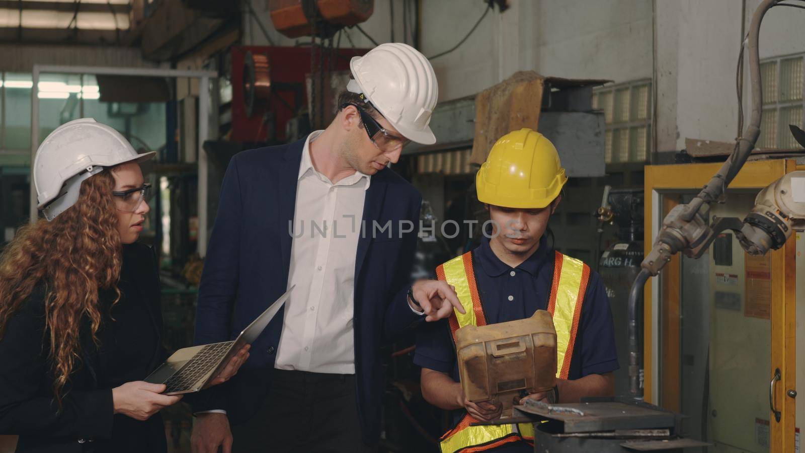 Three heavy industry business engineering in hardhats discuss information on laptop computer while standing indoors welding manufacturing industrial for check and control automated programming
