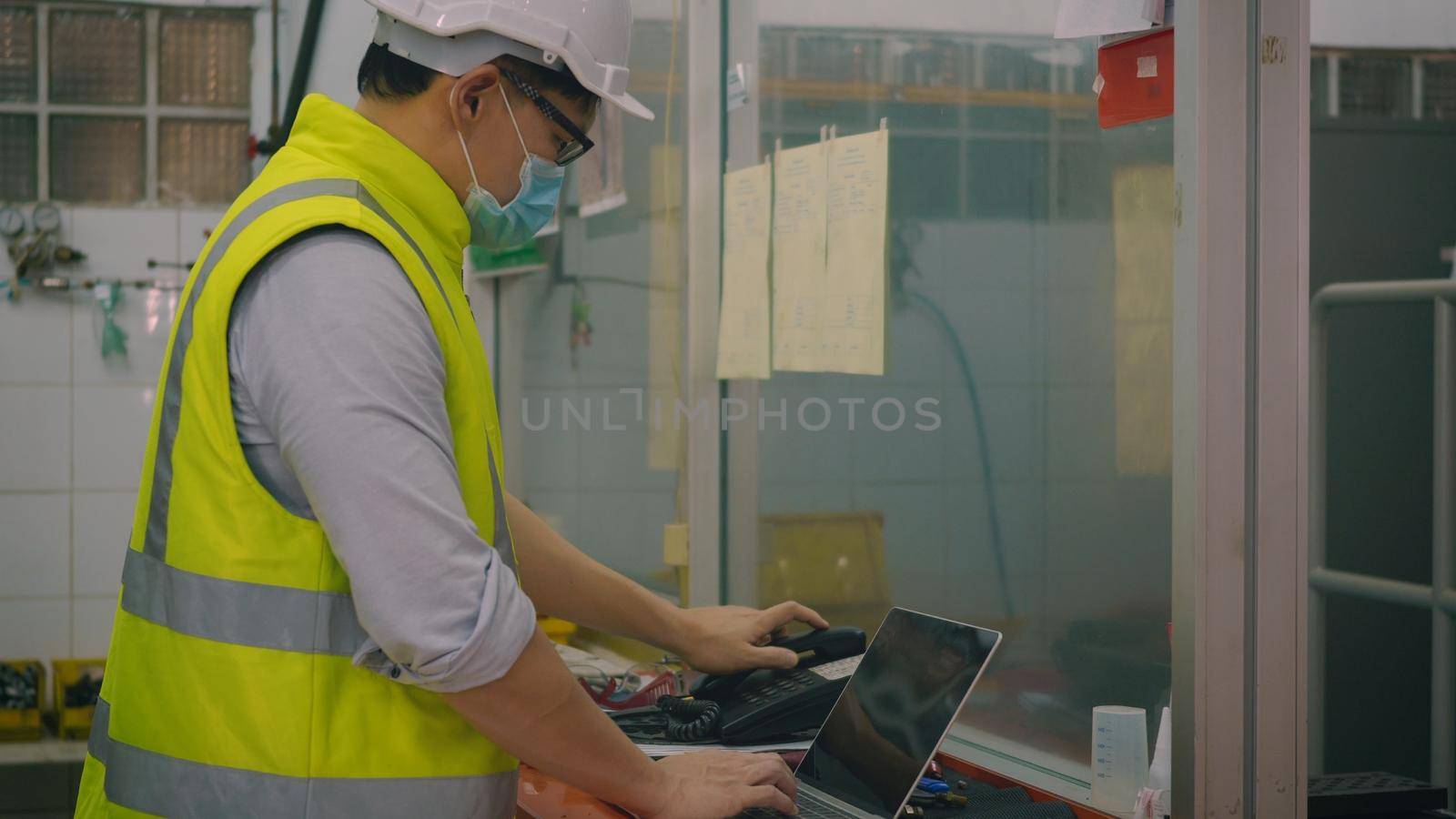 Asian factory worker man offering phone receiver as business communication, Technician man helmet at work in control room station talking on telephone,