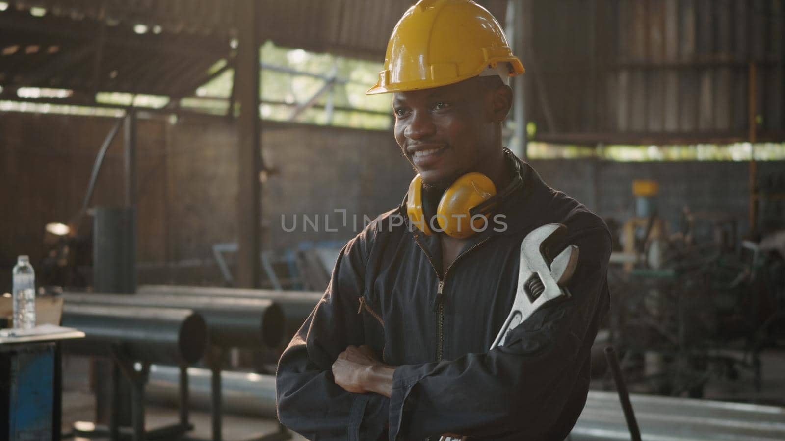 Portrait American industrial black young worker man smiling with yellow helmet in front machine, Engineer standing holding wrench tools and arms crossed at work in the industry factory.