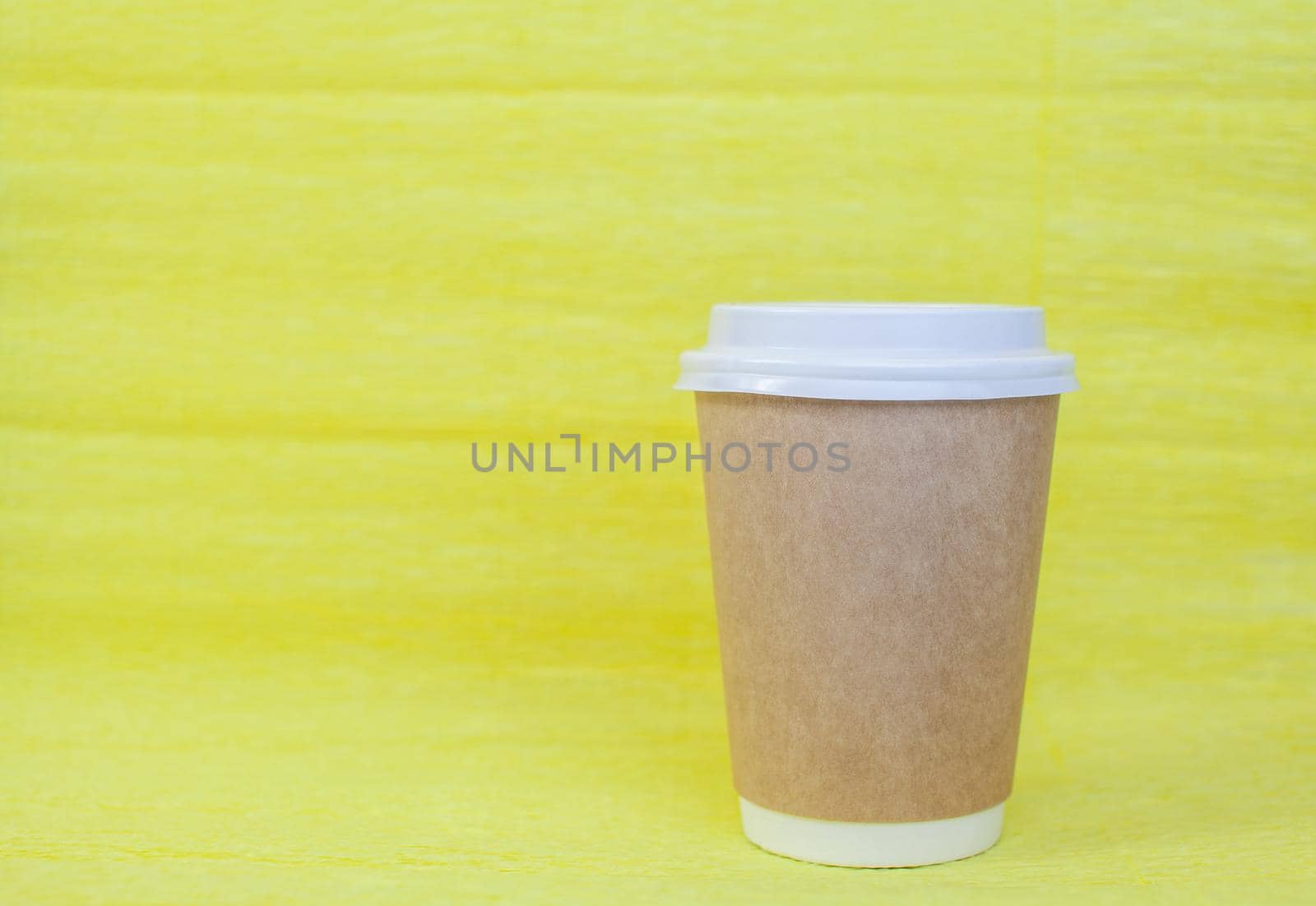 Paper cup of coffee closed with a white lid on a yellow background. There is a place for the text.