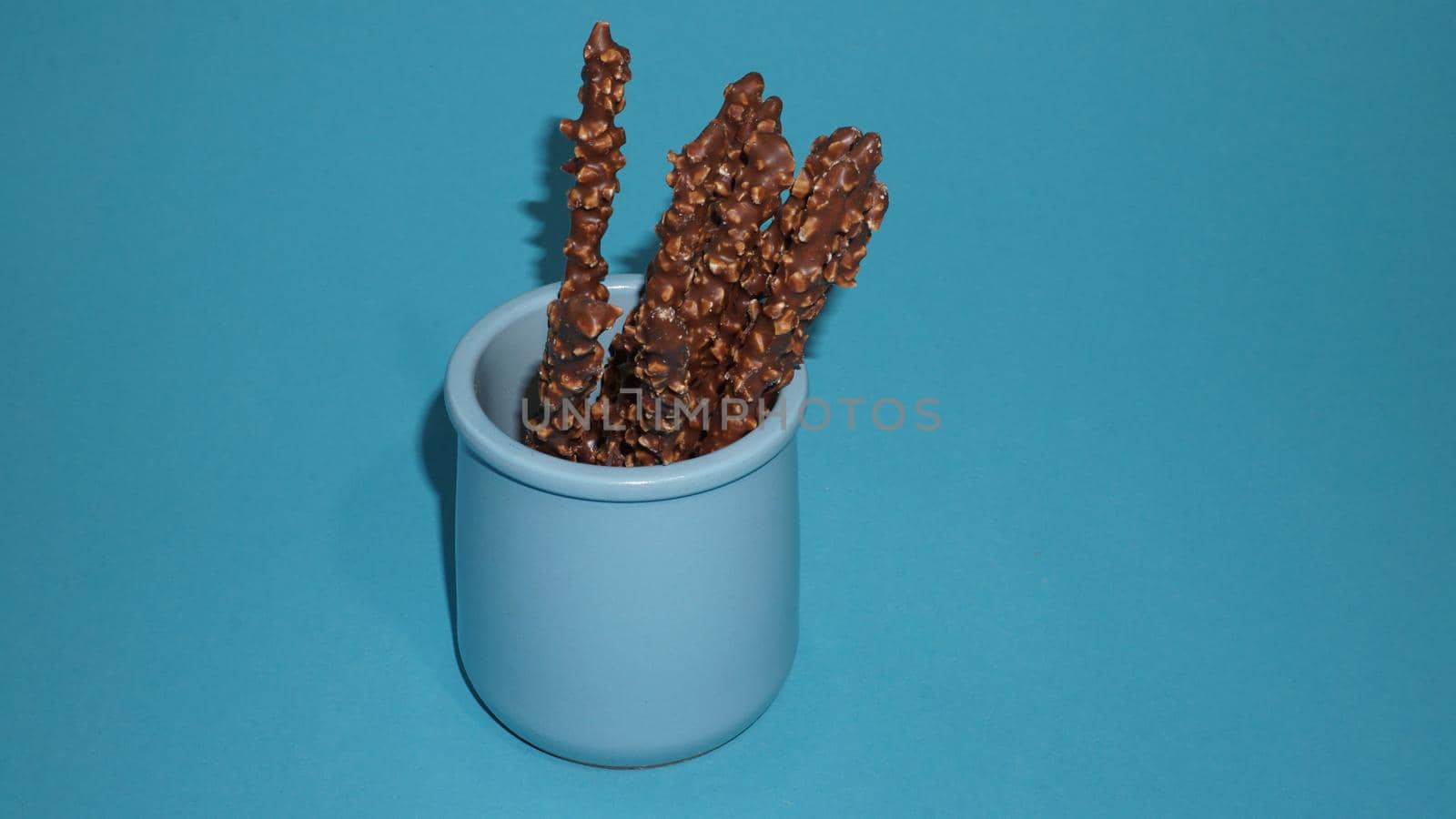 Chocolate crispy sticks with hazelnut sprinkles on a blue background.