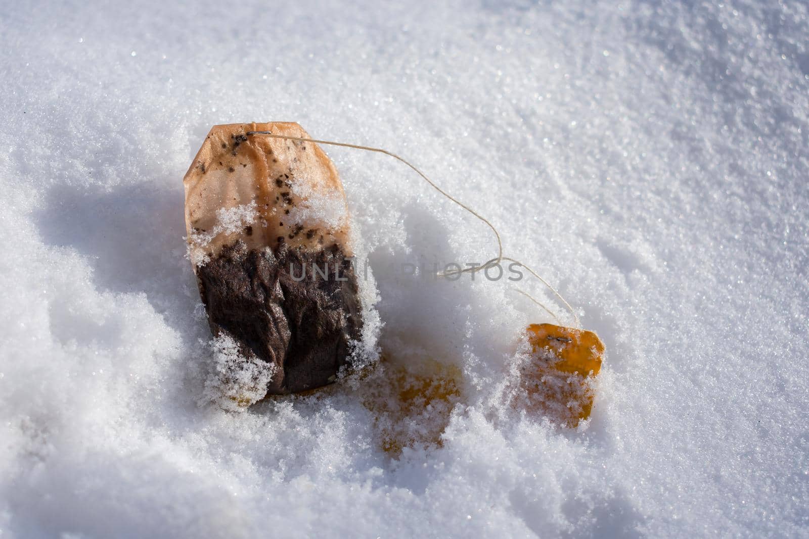 Thrown into the street A used tea bag lies in the snow and litters nature