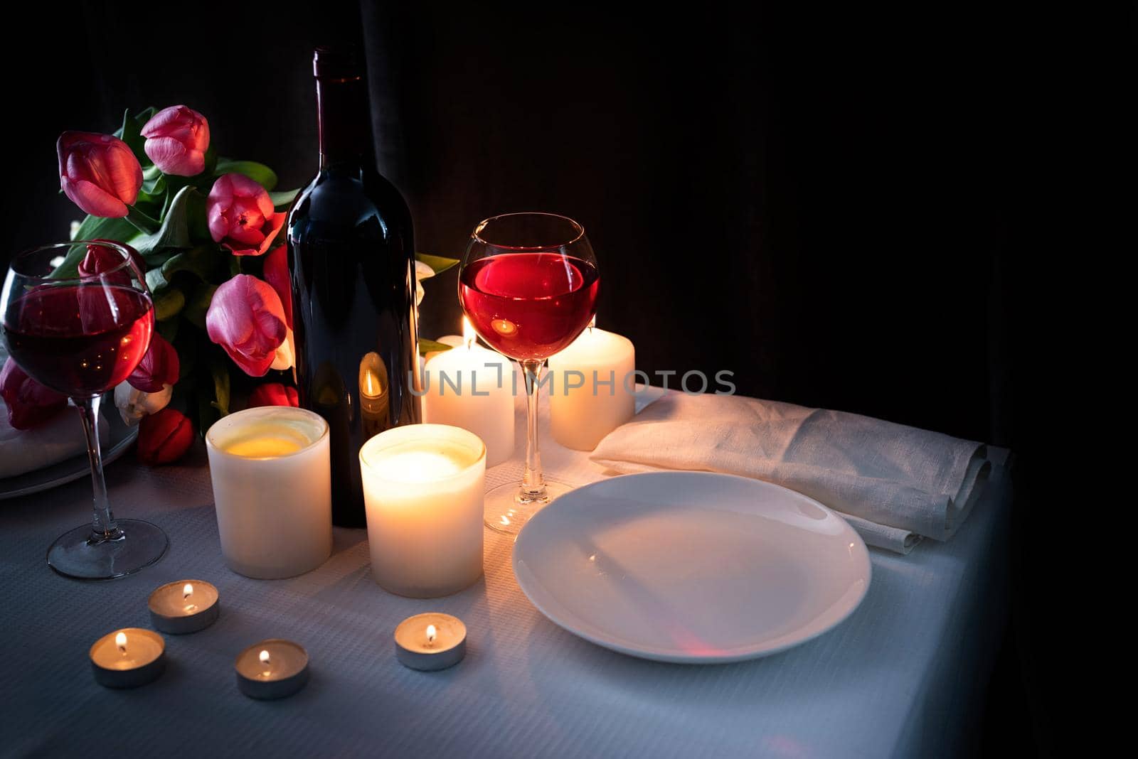 Romantic Candlelight Dinner for Two Lovers. Set of tableware with bouquet of tulips, wine and candles, dark background