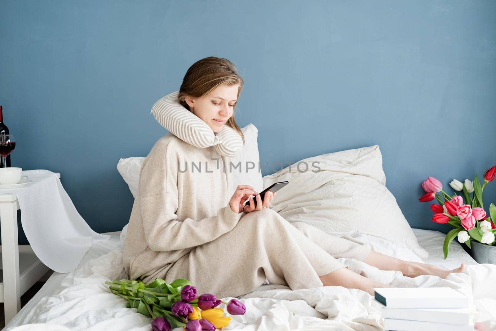 Happy woman sitting on the bed wearing pajamas typing a message on the phone by Desperada