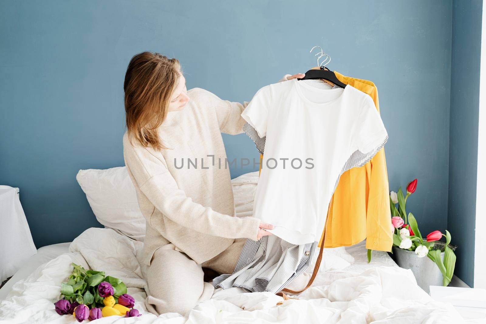 Young smiling woman organizing clothes sitting on the bed at home