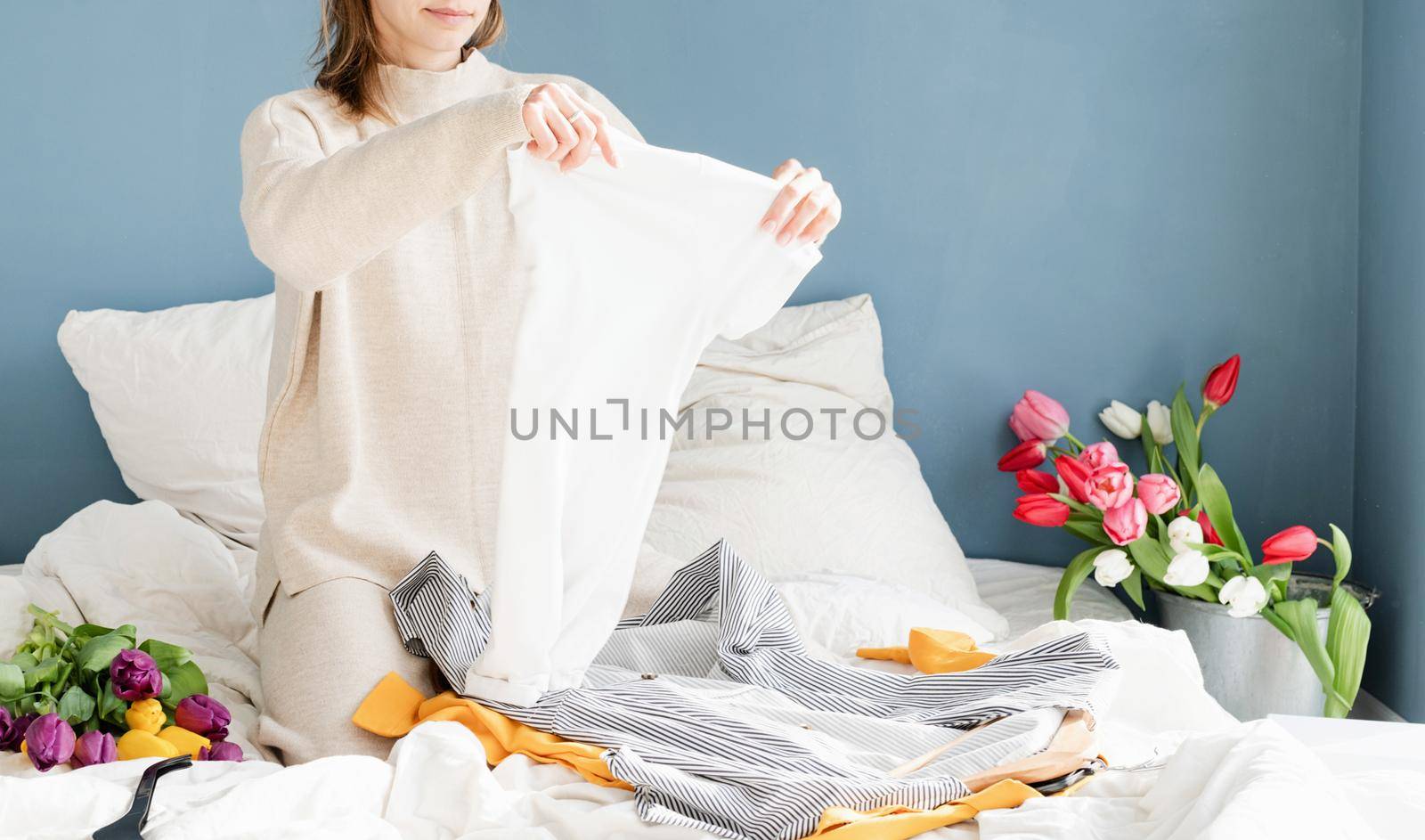 Young smiling woman organizing clothes sitting on the bed at home