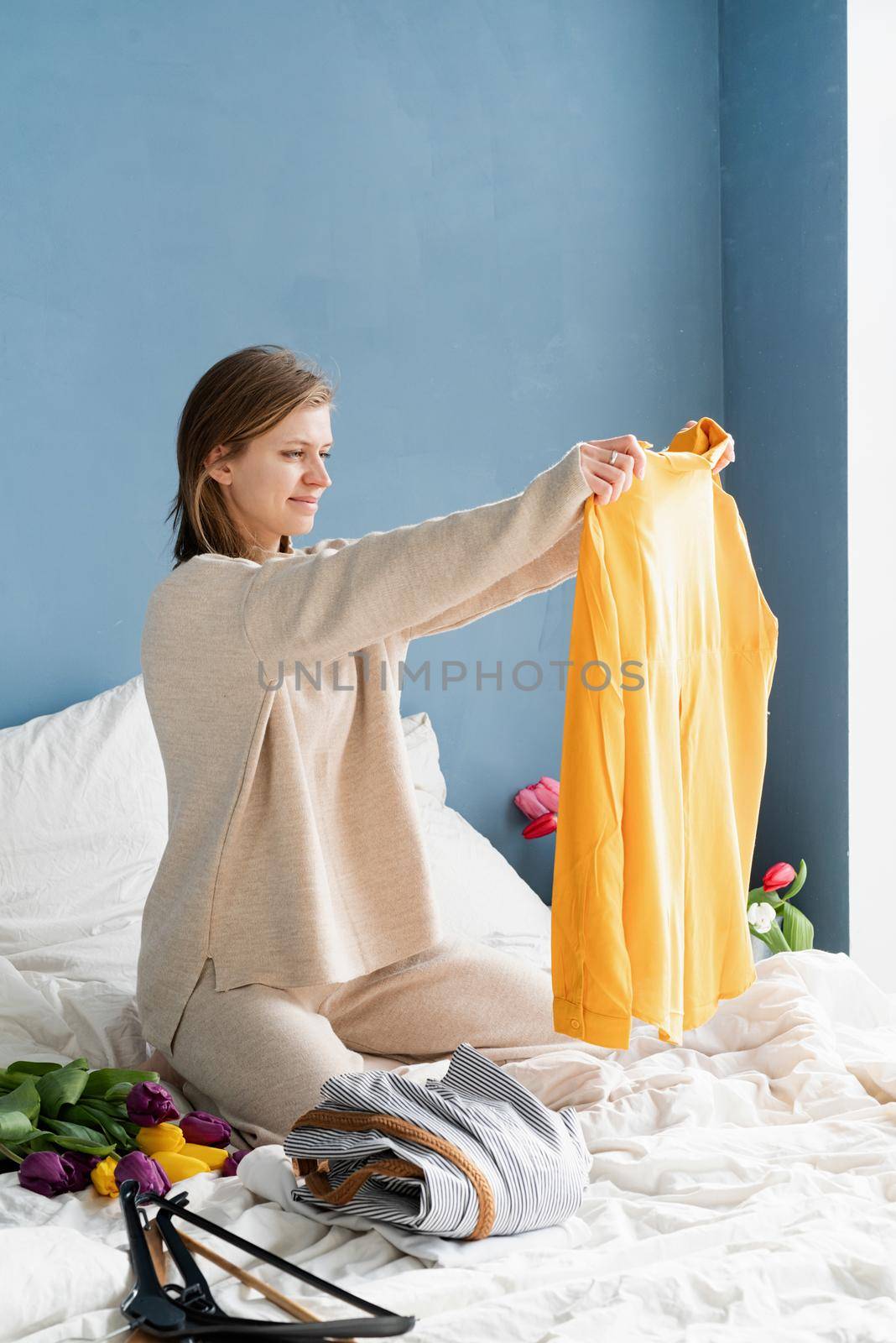 Young smiling woman organizing clothes sitting on the bed at home