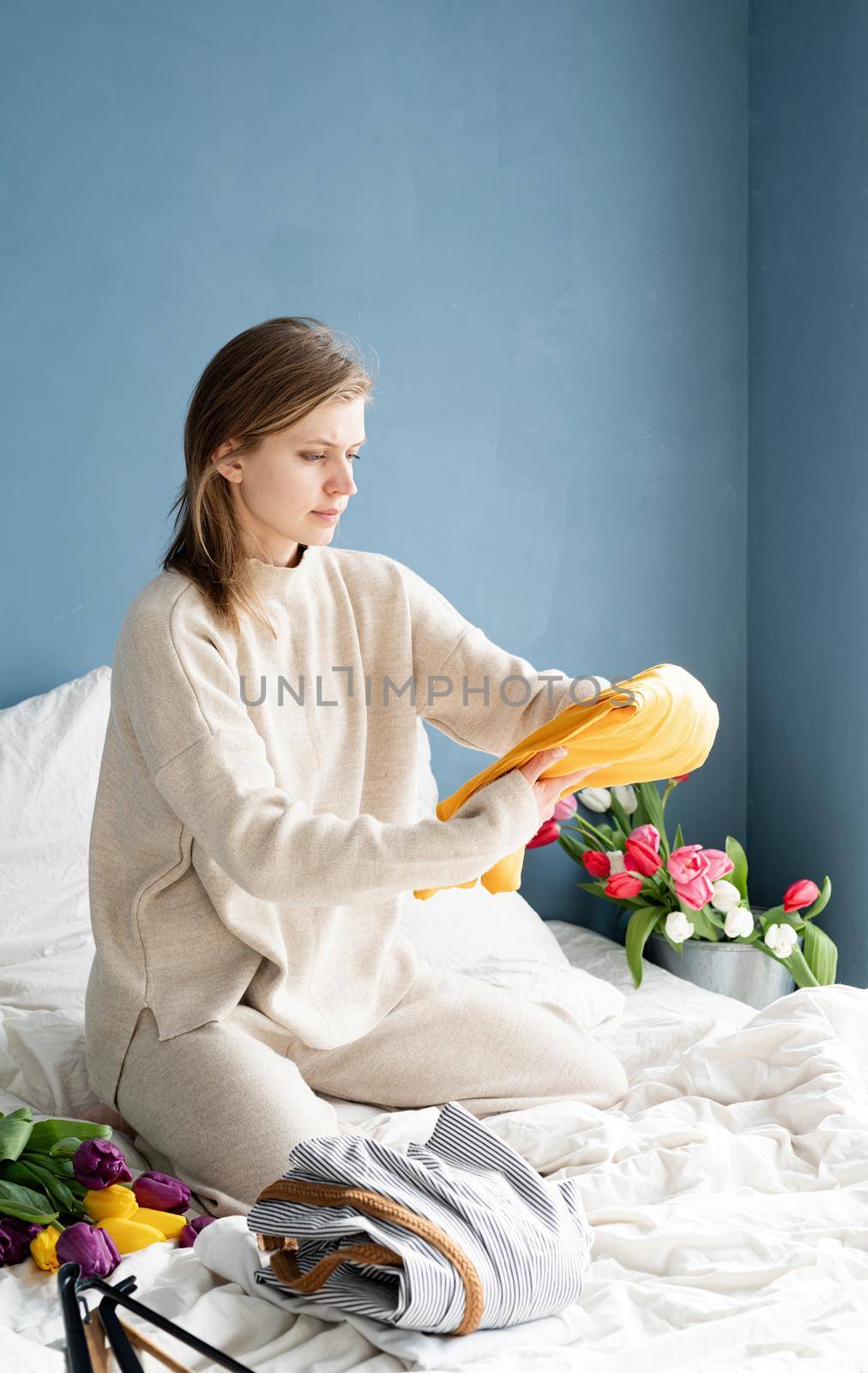 Young smiling woman organizing clothes sitting on the bed at home