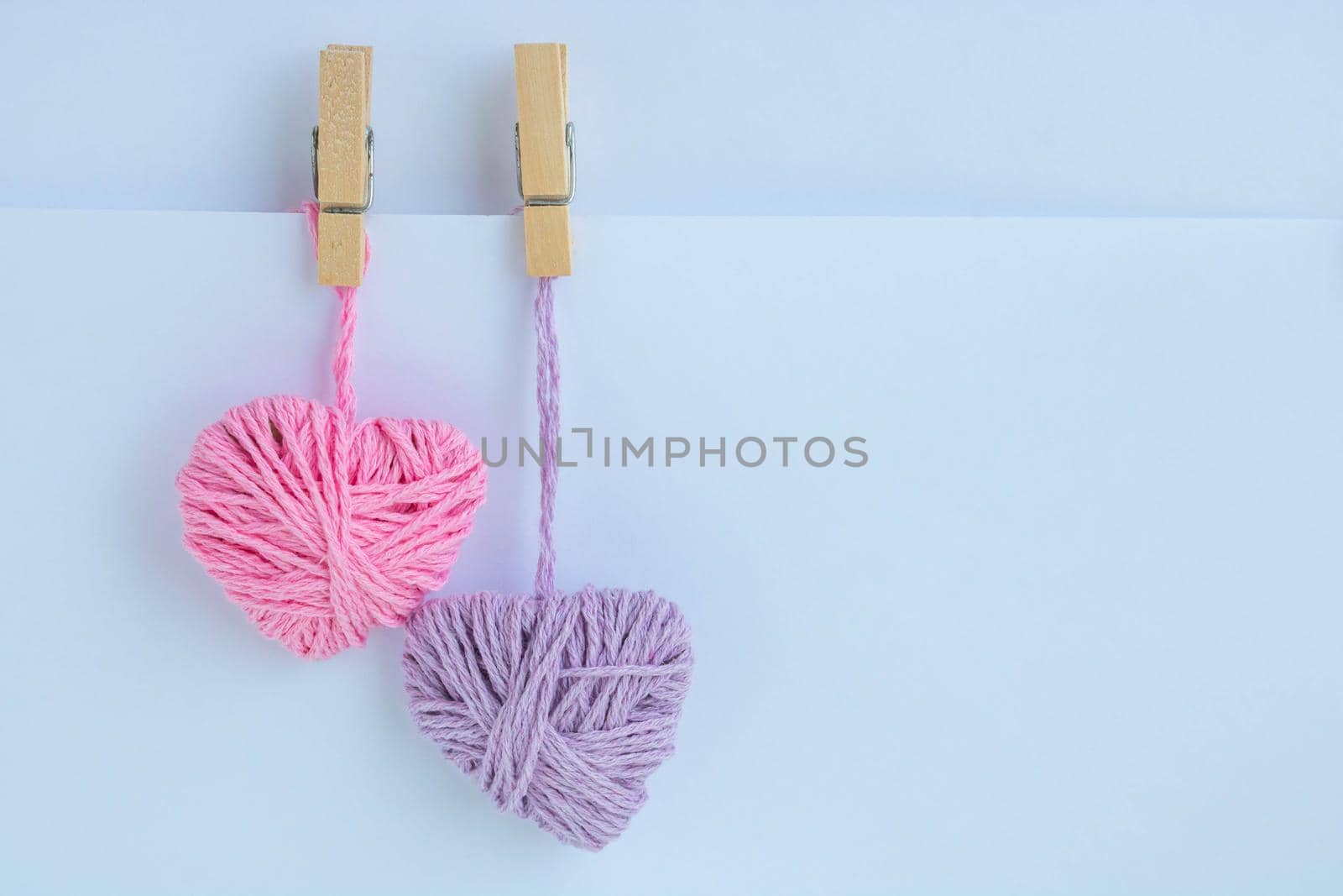 Two hearts of thread hang with clothespins on a paper pocket. Holiday card, background. The concept of Valentine's Day, March 8, Mother's Day.