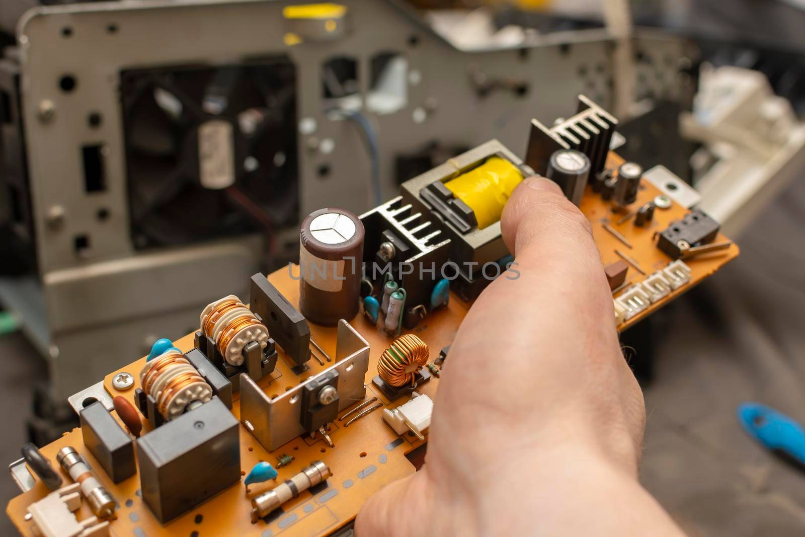 view of the electronic board, the power supply circuit of the device with radio components in the hand of a person, the master of the service center against the background of disassembled faulty equipment, office printer