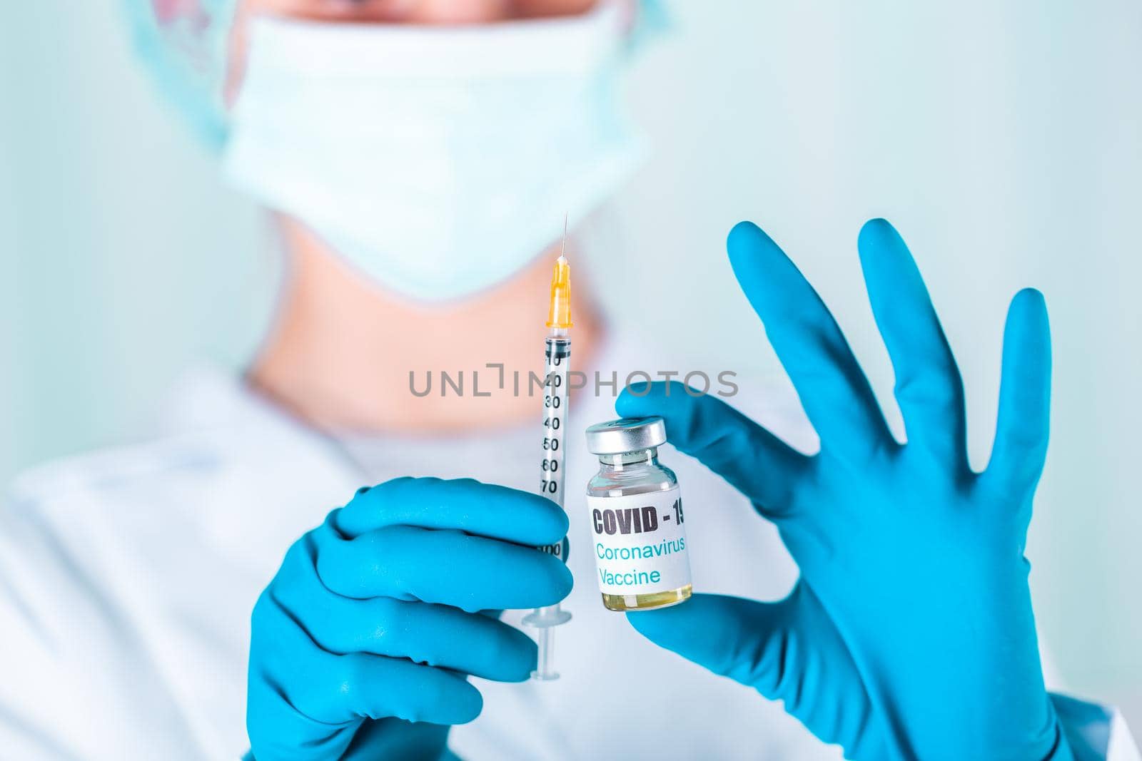 Woman doctor or nurse in uniform and gloves wearing face mask protective in lab, holding medicine vial vaccine bottle with COVID-19 Coronovirus vaccine label