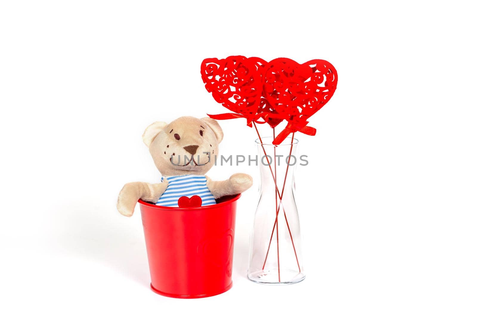 Soft toy bear with an embroidered heart in a red metal bucket on a white background. The concept of a gift to a woman for valentine's day, a symbol of love