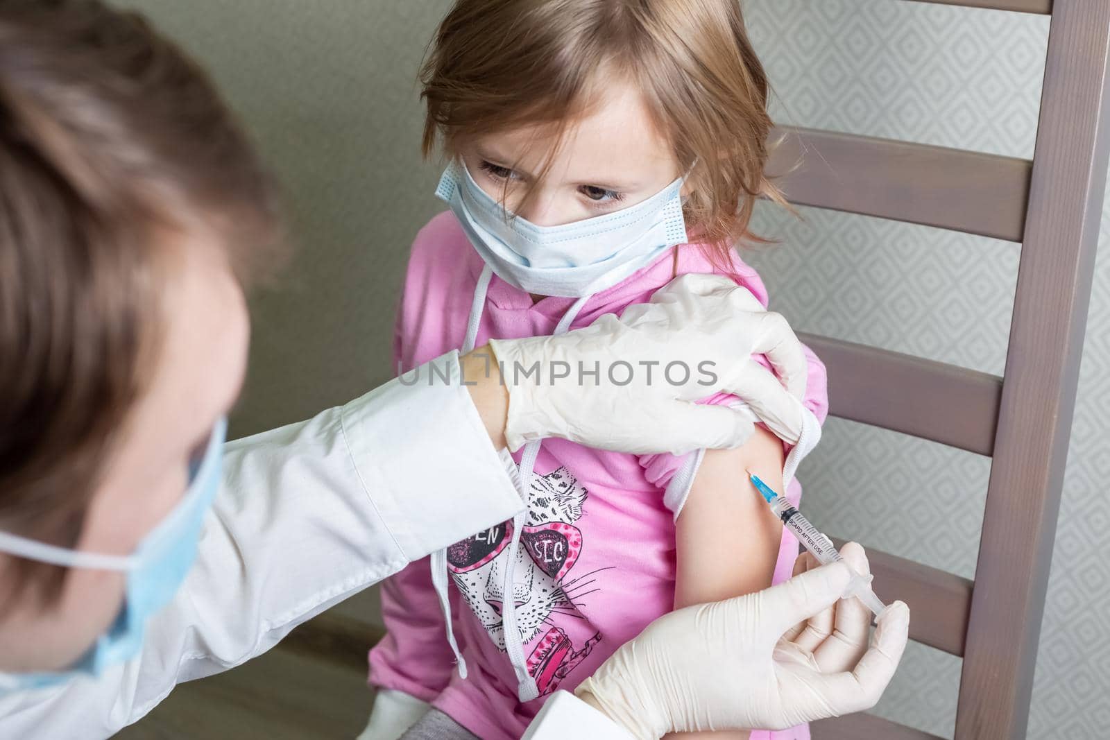 Little caucasian girl in a medical mask sits and receives a vaccine by galinasharapova