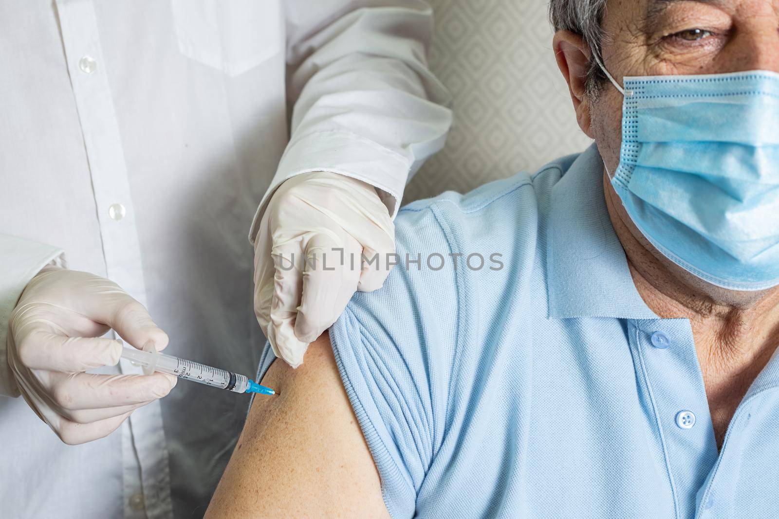 An elderly Caucasian man receives a dose of vaccination in a nursing home, doctor holding syringe subcutaneous vaccine for adults.