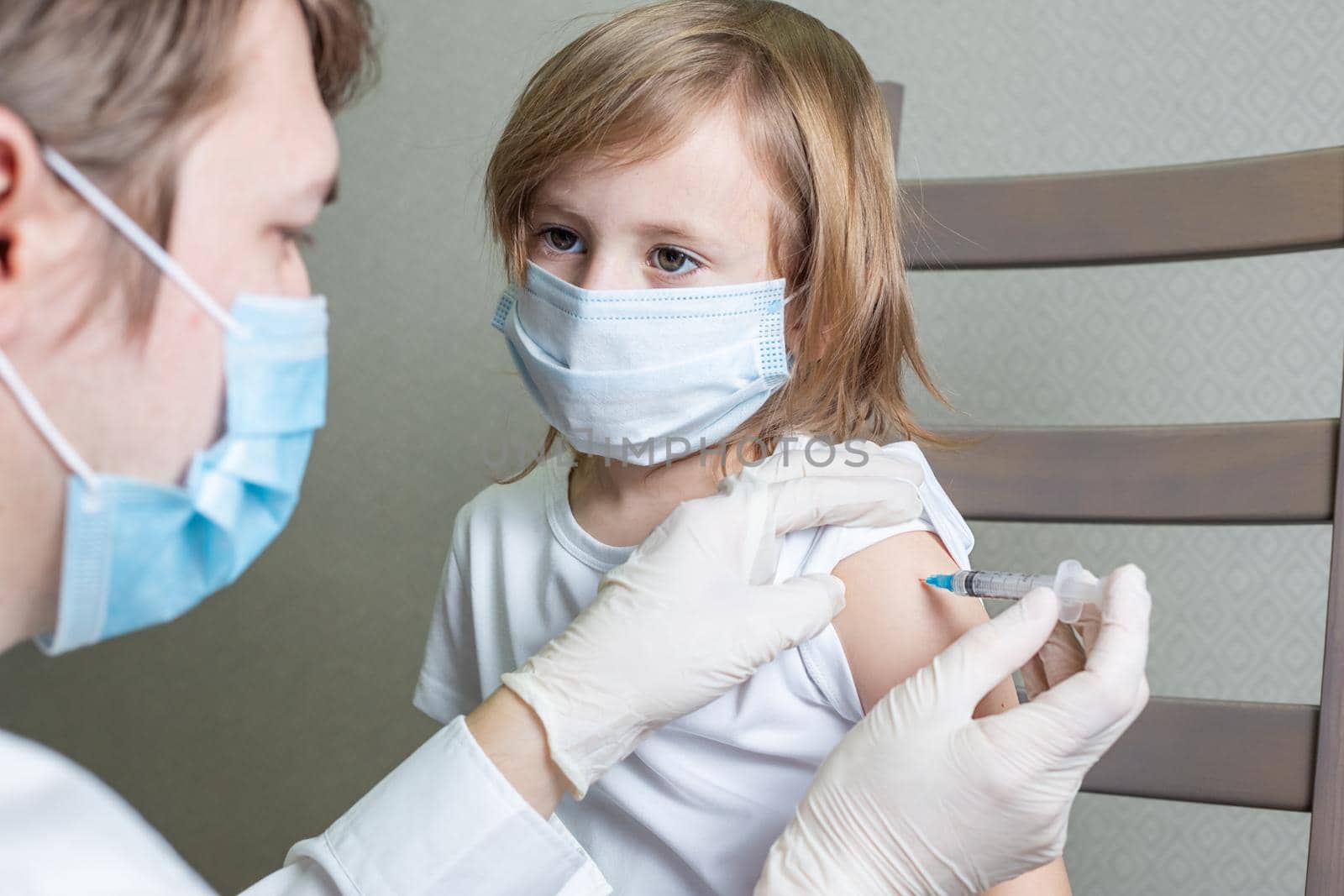 Doctor in mask and gloves makes an injection in the shoulder of a little girl by galinasharapova