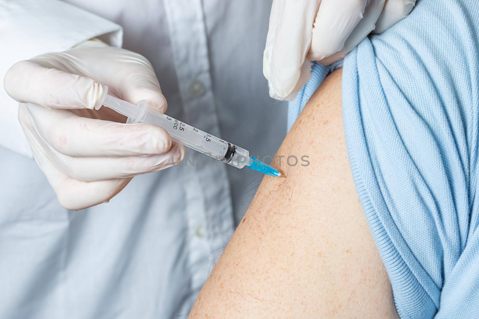 An elderly Caucasian man receives a dose of vaccination in a nursing home, doctor holding syringe subcutaneous vaccine for adults.