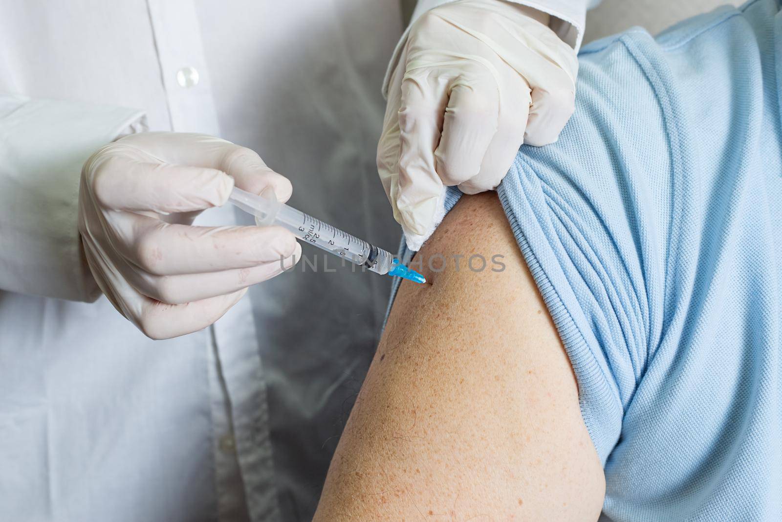 An elderly Caucasian man receives a dose of vaccination in a nursing home, doctor holding syringe subcutaneous vaccine for adults.