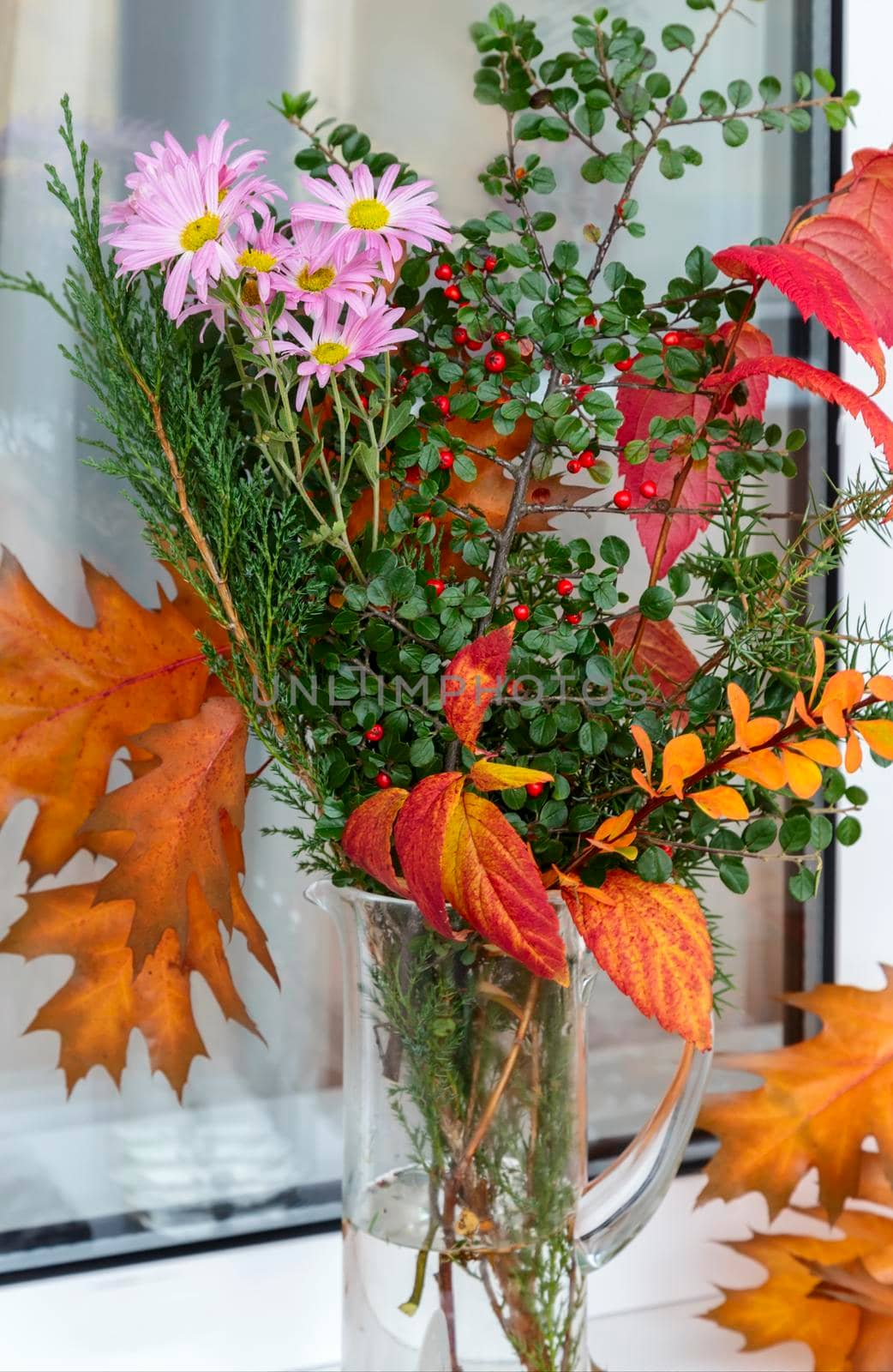 On the window sill in a glass decanter beautiful autumn bouquet of flowers and bright autumn leaves.