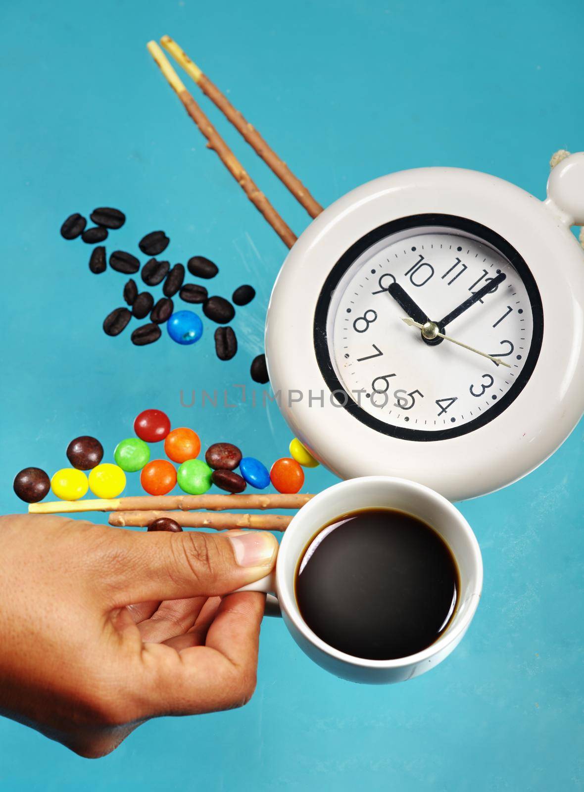Man hand holding espresso cup with alarm clock on confectionery and sweet candy background. by noppha80