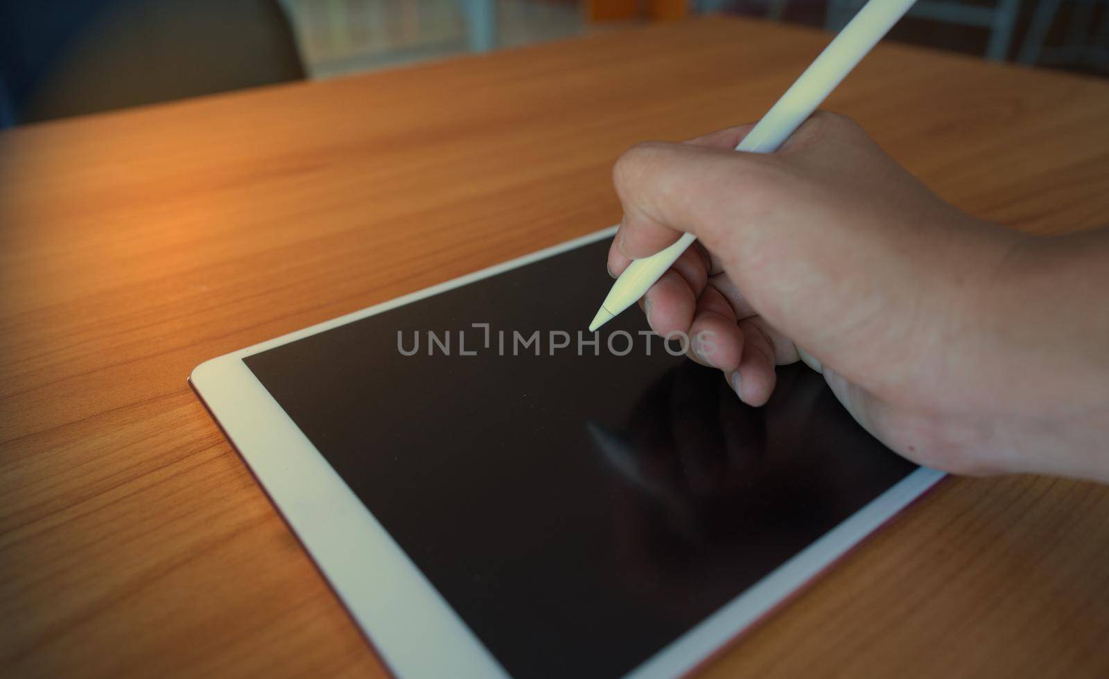 A man writing on the tablet with an electronic pencil on a wooden table