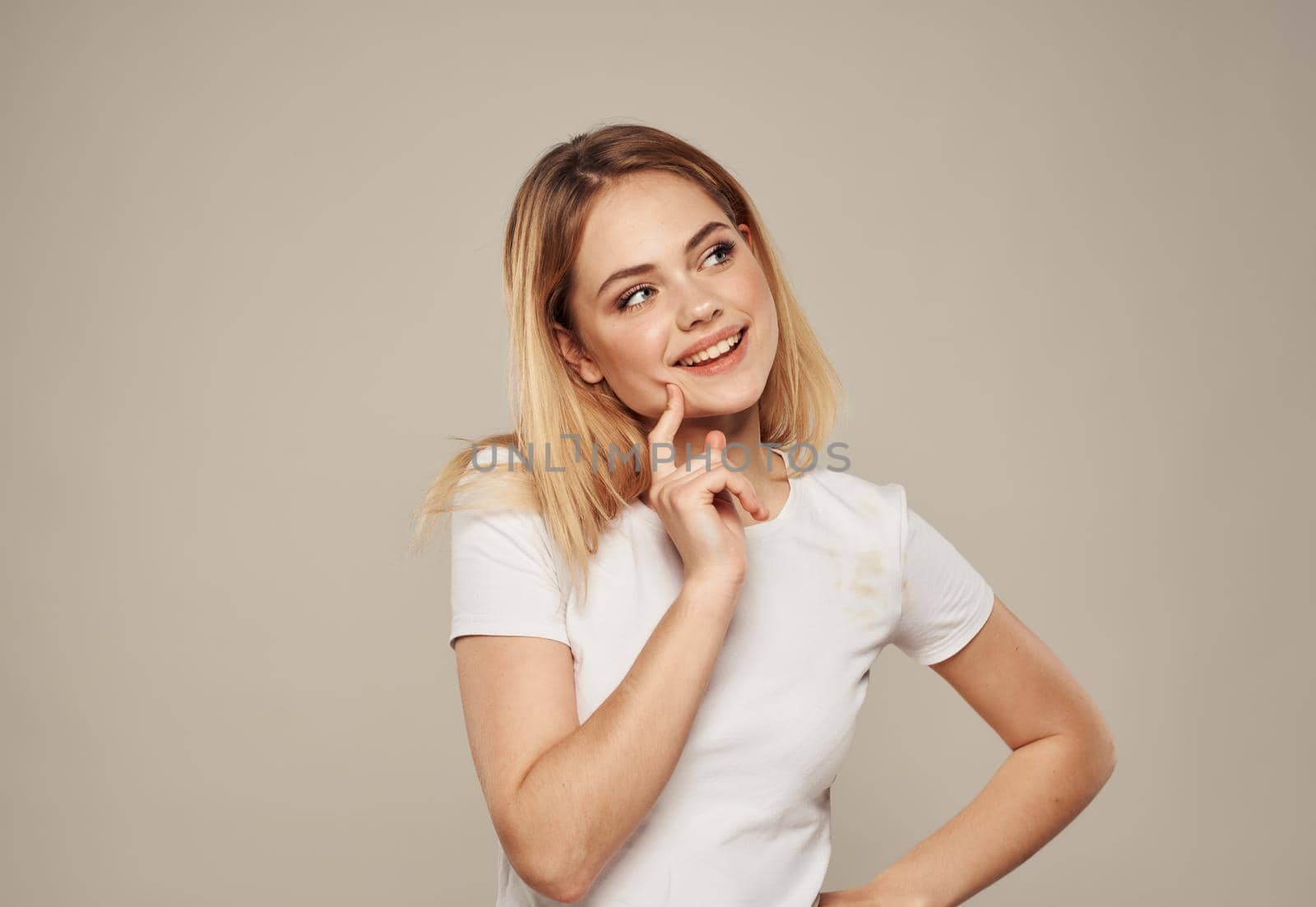 Pretty blonde in a white T-shirt on a beige background touches her face with her hand cropped view by SHOTPRIME