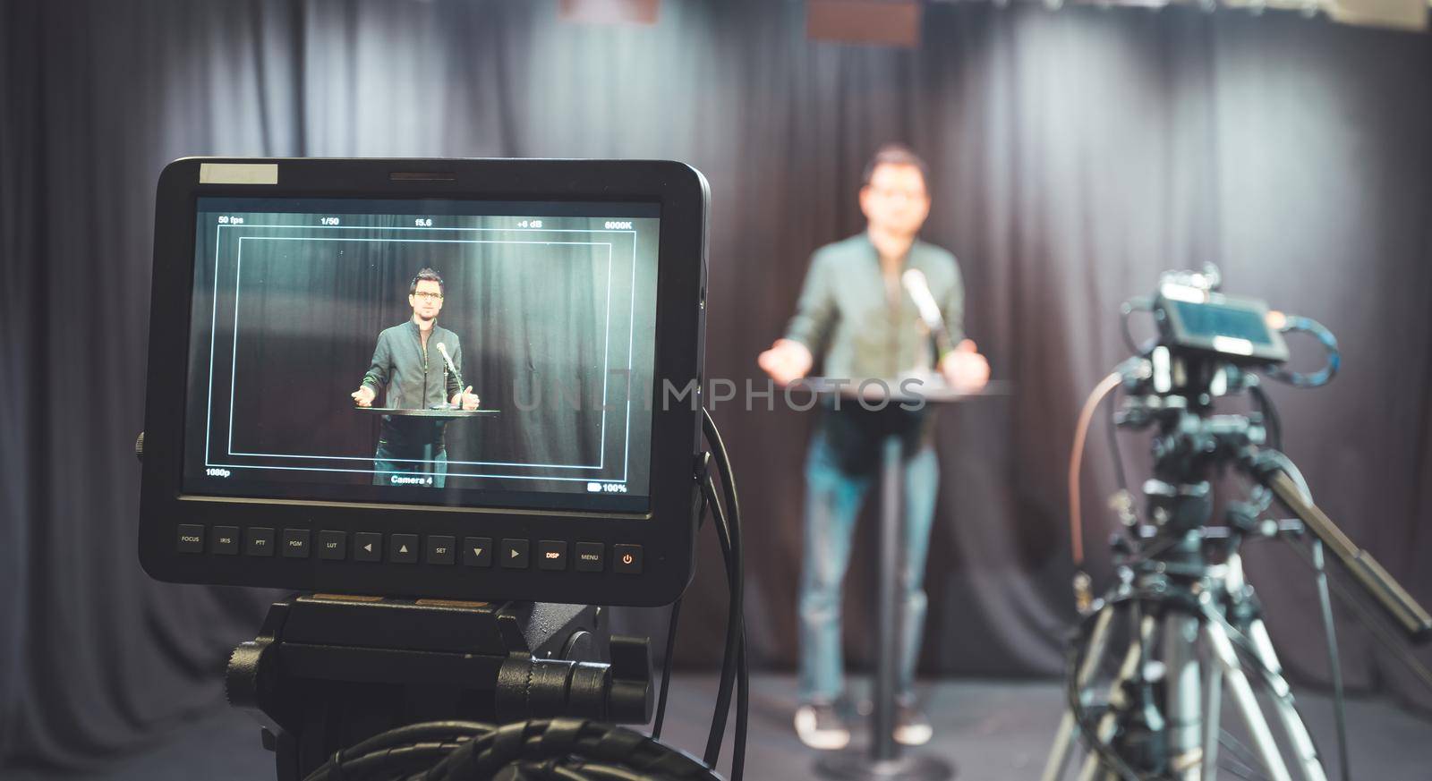 Young journalist in a television recording studio is talking into a microphone, blurry film cameras by Daxenbichler